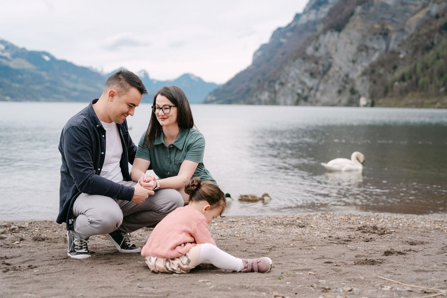 Family relaxes on rocky beach shore with mountain backdrop.