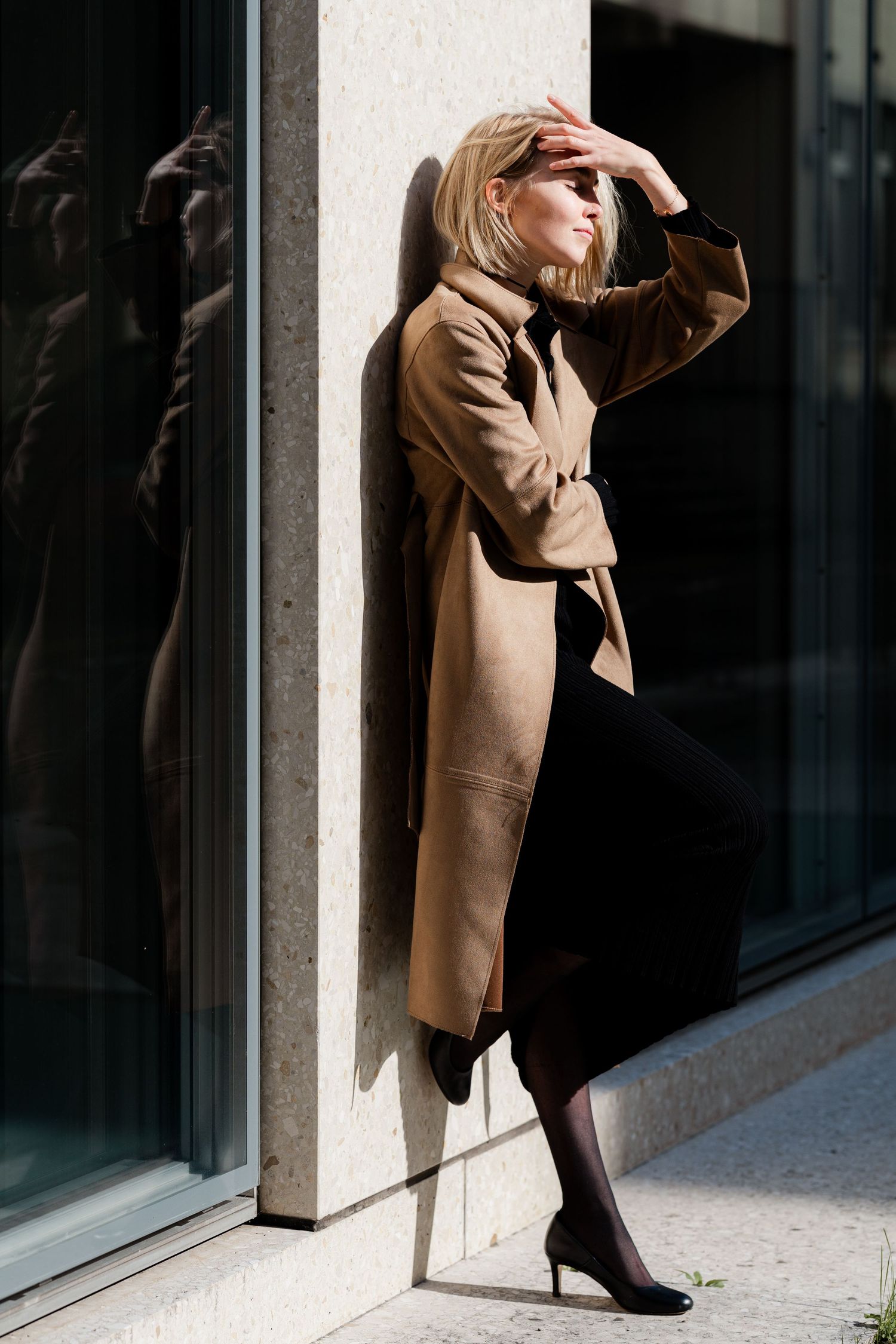 Elegant poses against modern architecture showcase a classic camel coat.