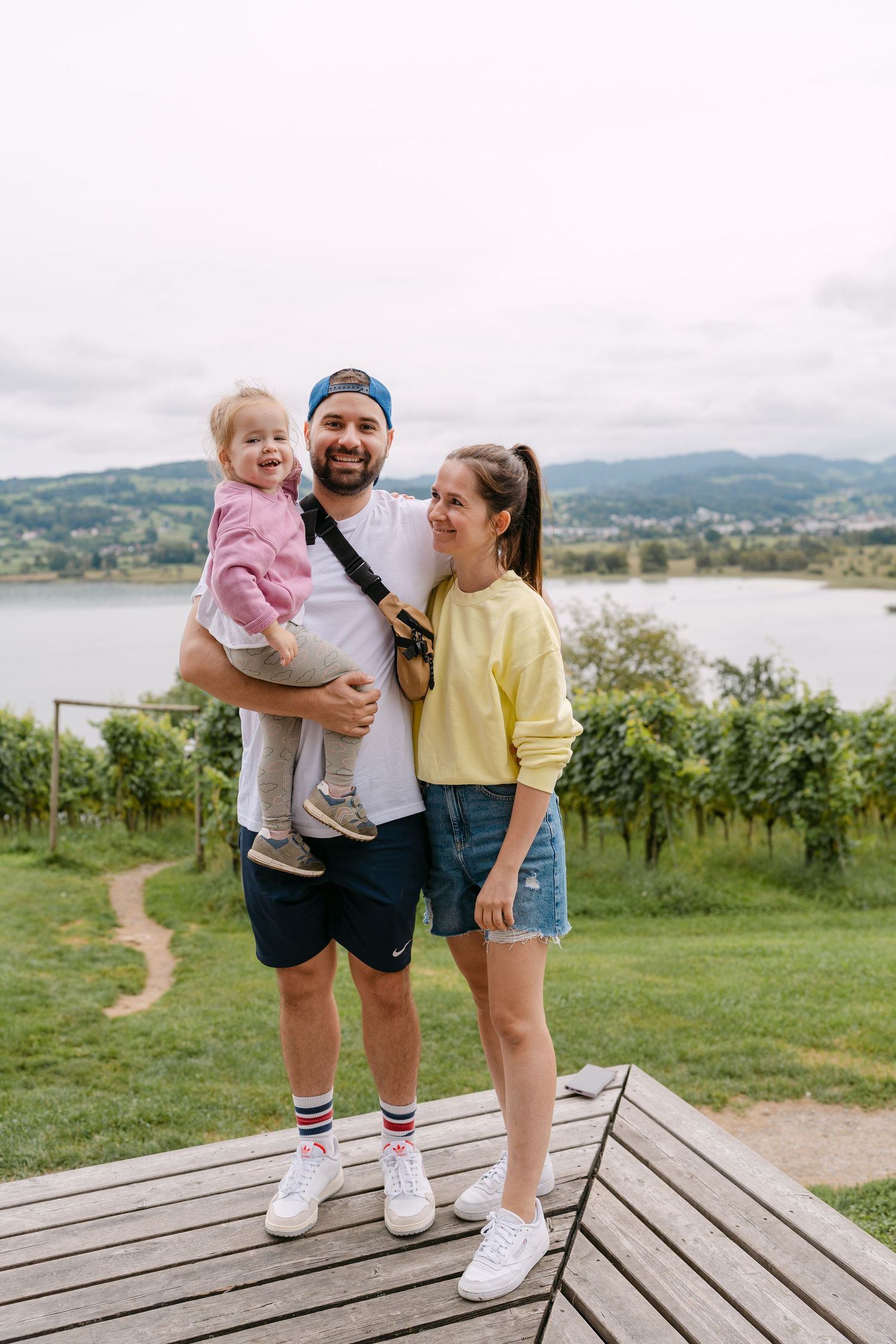 Family embracing on wooden platform overlooking scenic lake and mountains.