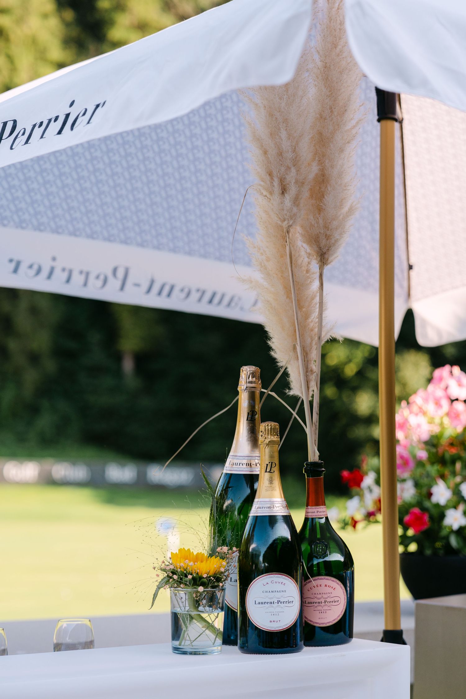 Laurent-Perrier champagne display with pampas grass decoration and pink flowers under white branded umbrella.