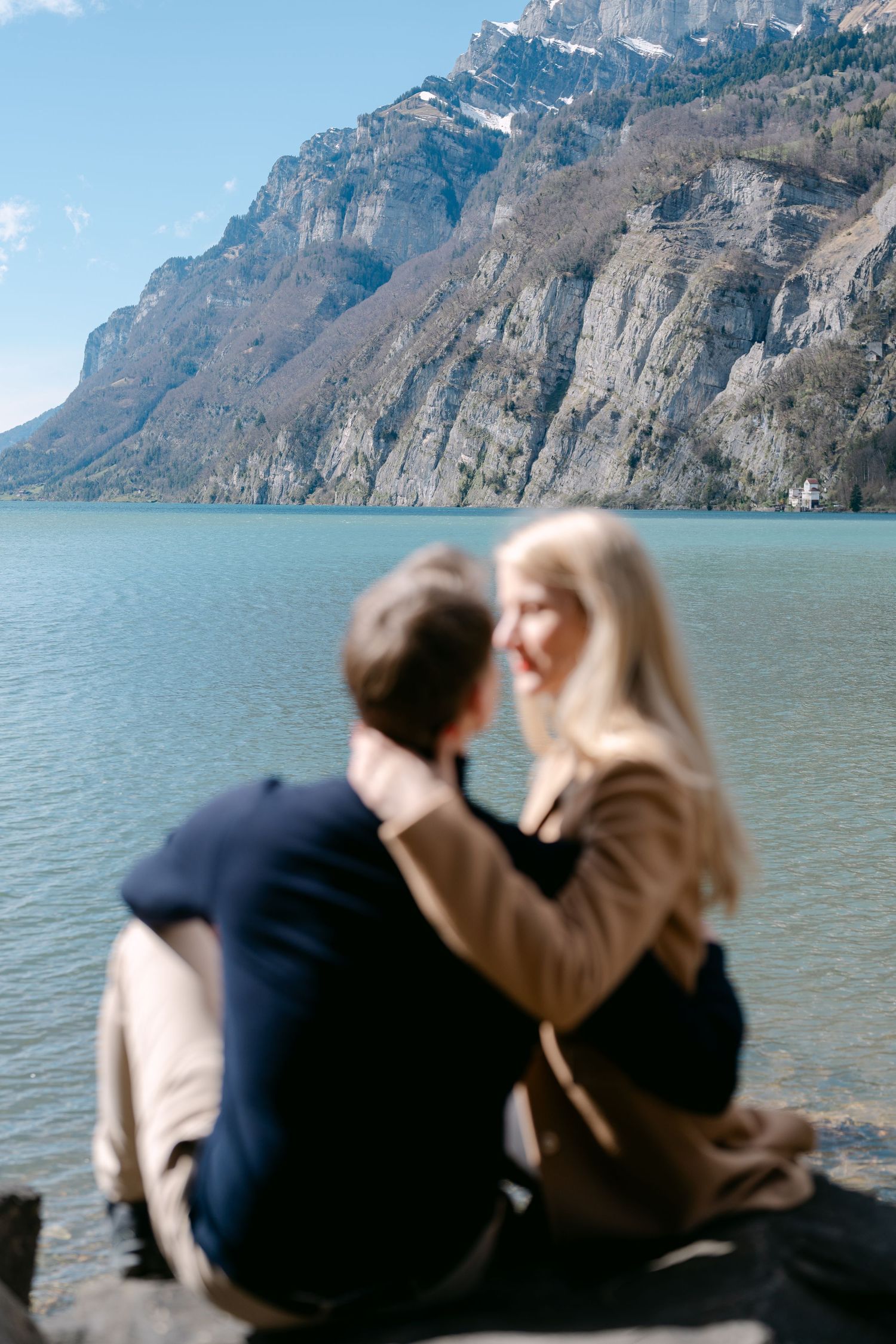 Couple relaxing by mountain lake with dramatic cliffs in background.