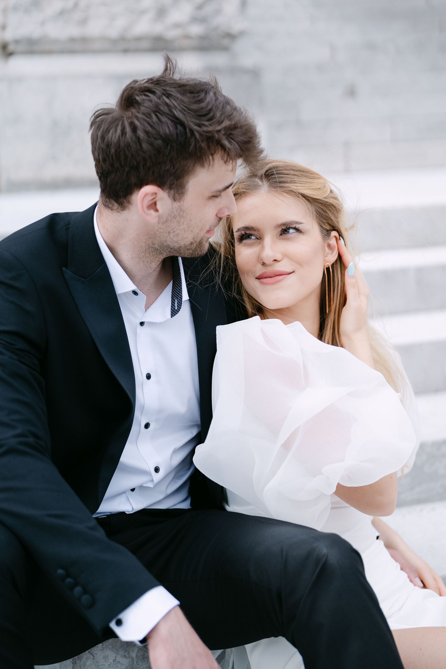 Romantic wedding couple shares intimate moments on marble steps in elegant formal attire.