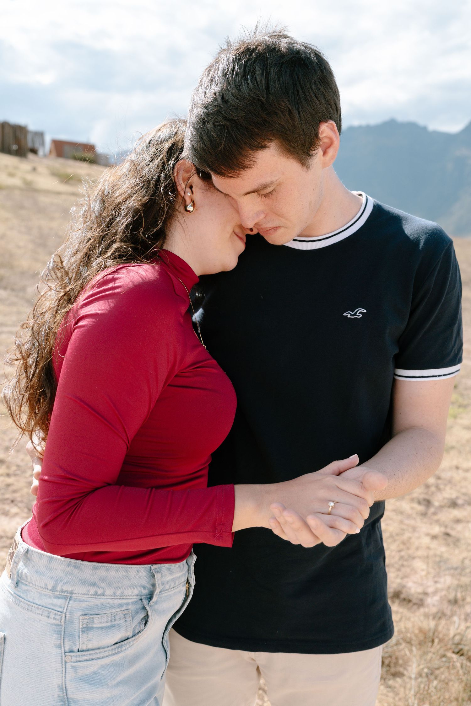 Tender moments between a couple in red and black clothing against a mountain landscape.