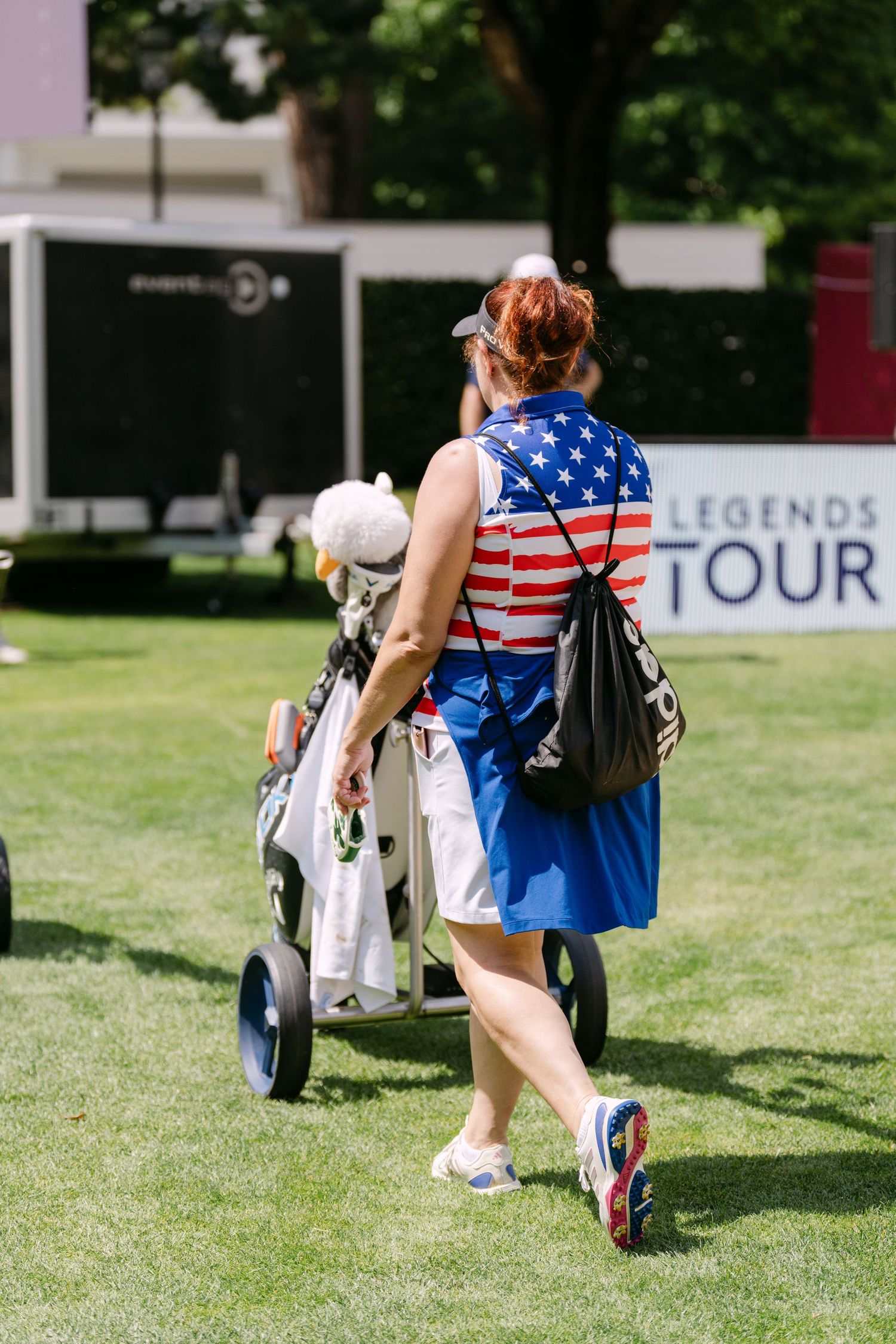 Spectators wearing American flag attire watch a golf tournament on a sunny day.
