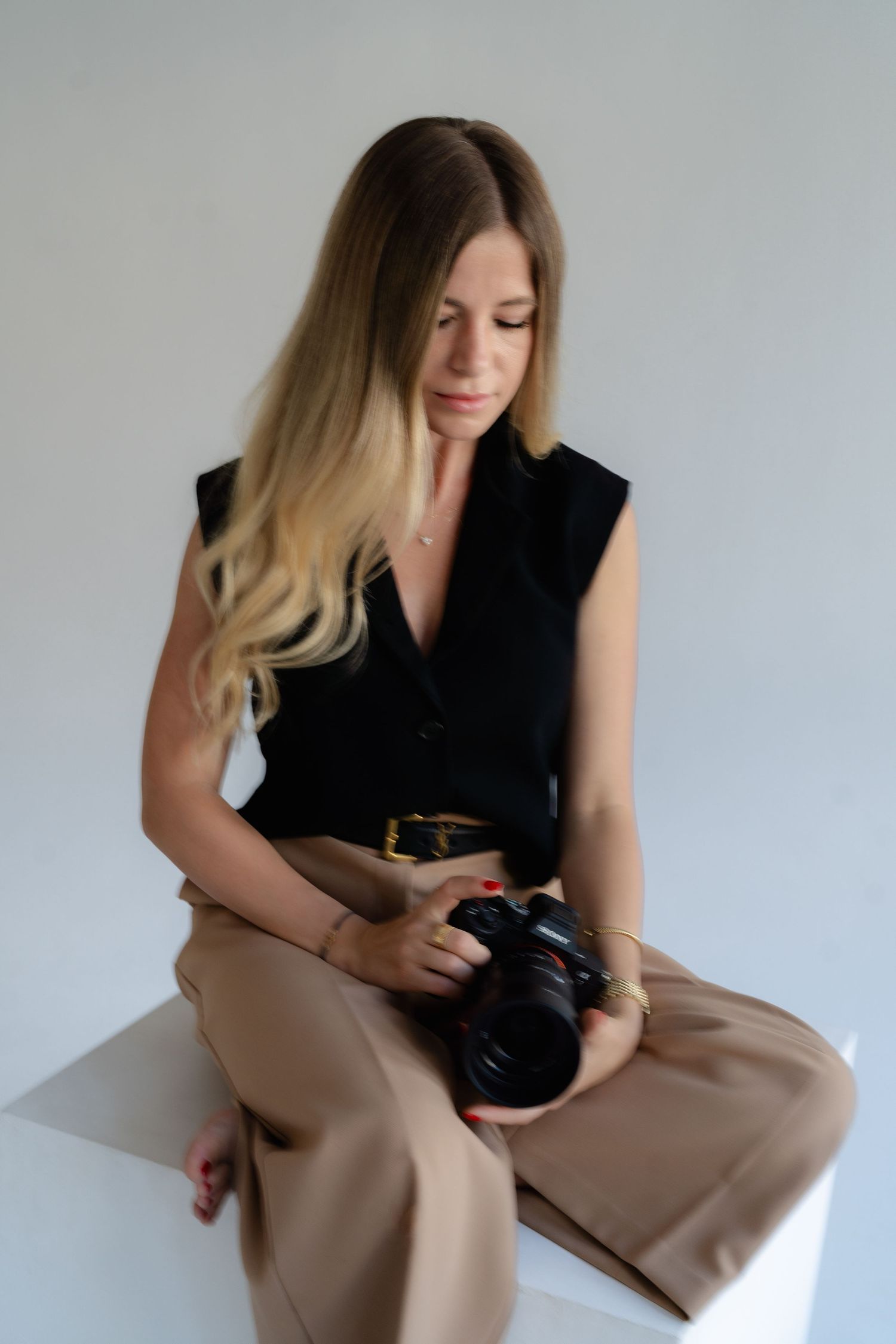 Person in black top reviewing photos on digital camera against neutral background.