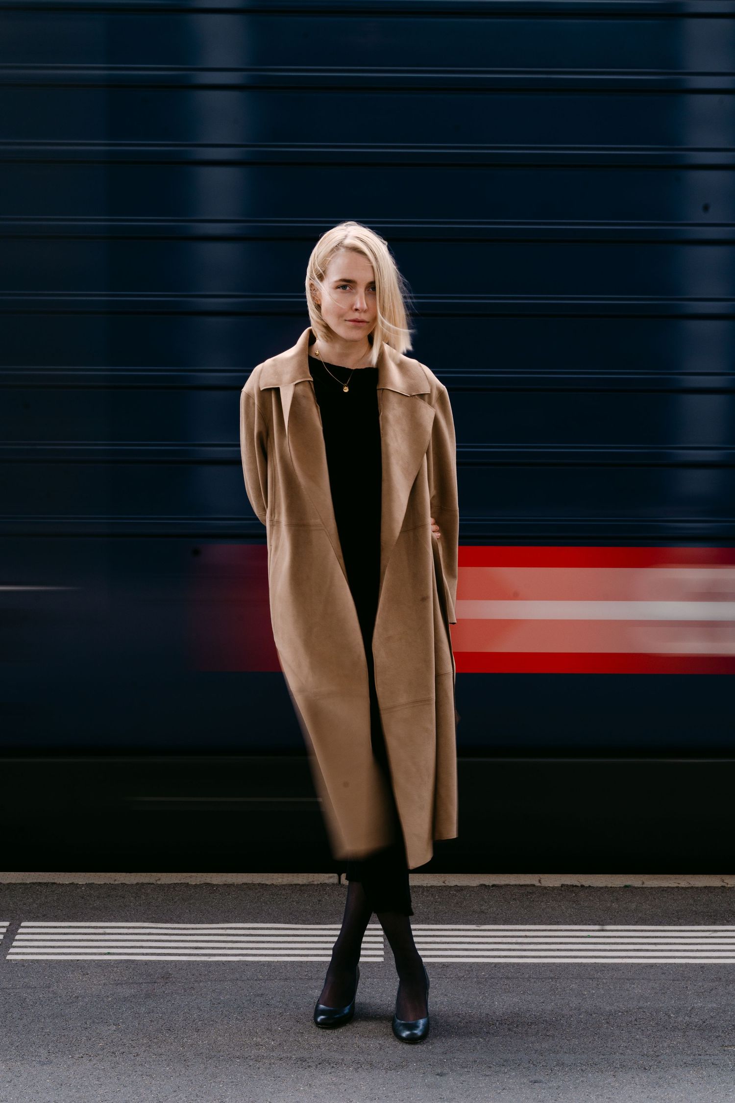 Fashion photo of a camel coat against a dark wall with red accent lighting.
