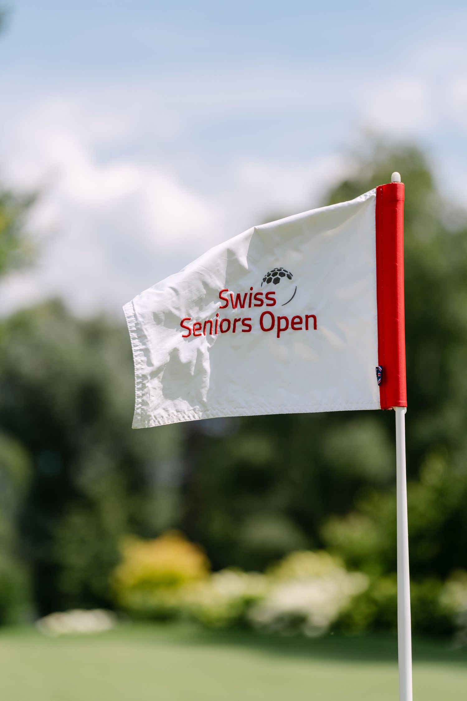 White flag with 'Swiss Seniors Open' text fluttering in the breeze on a golf course.