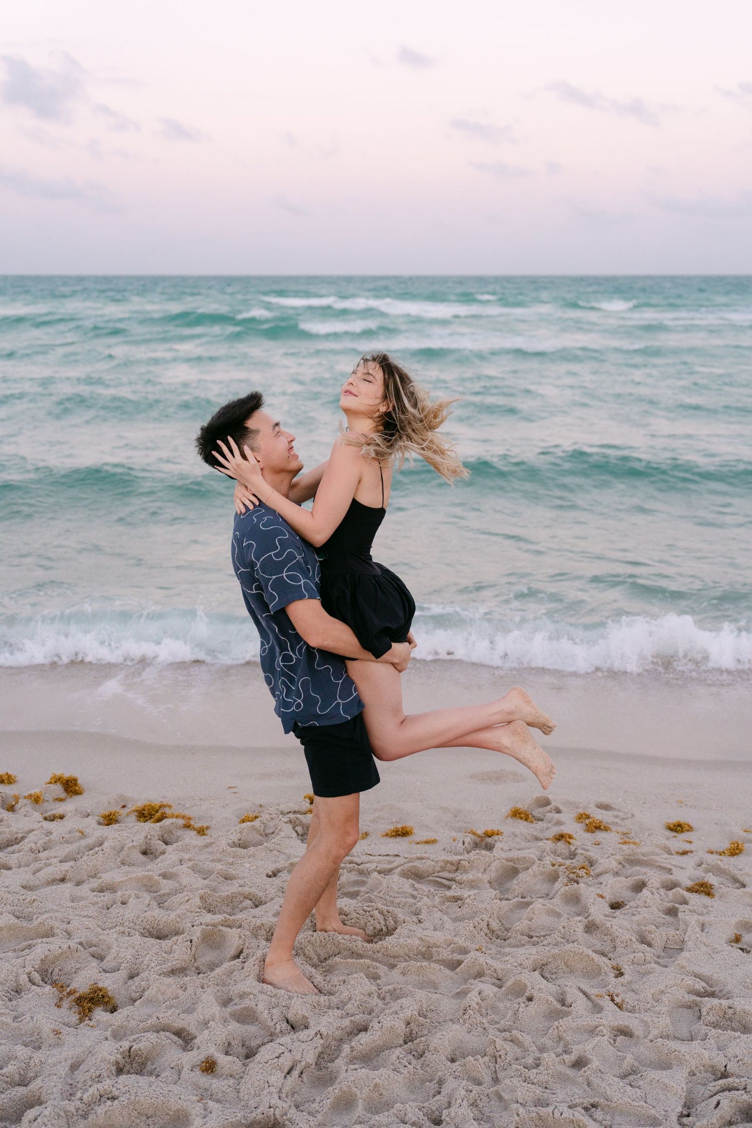 A couple spins and laughs together during a romantic beach photoshoot.