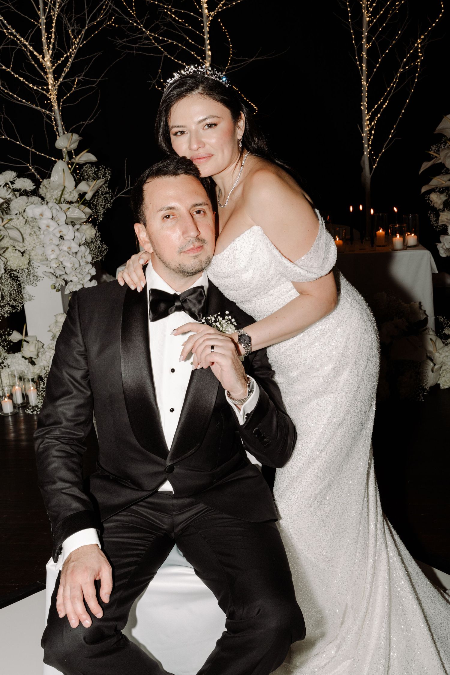 Elegant couple poses intimately against backdrop of twinkling lights at evening reception.