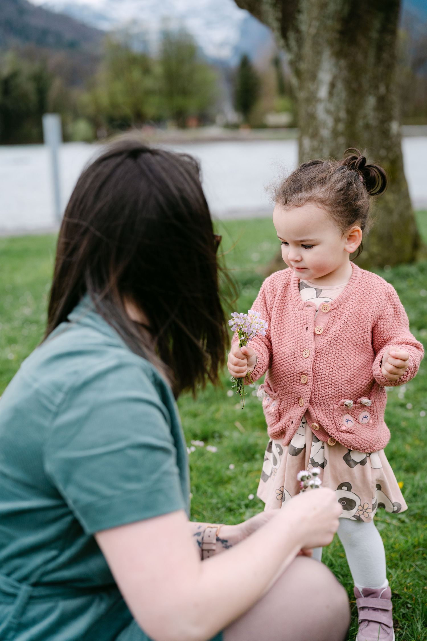 A small child in a pink cardigan interacting with someone on a grassy area.