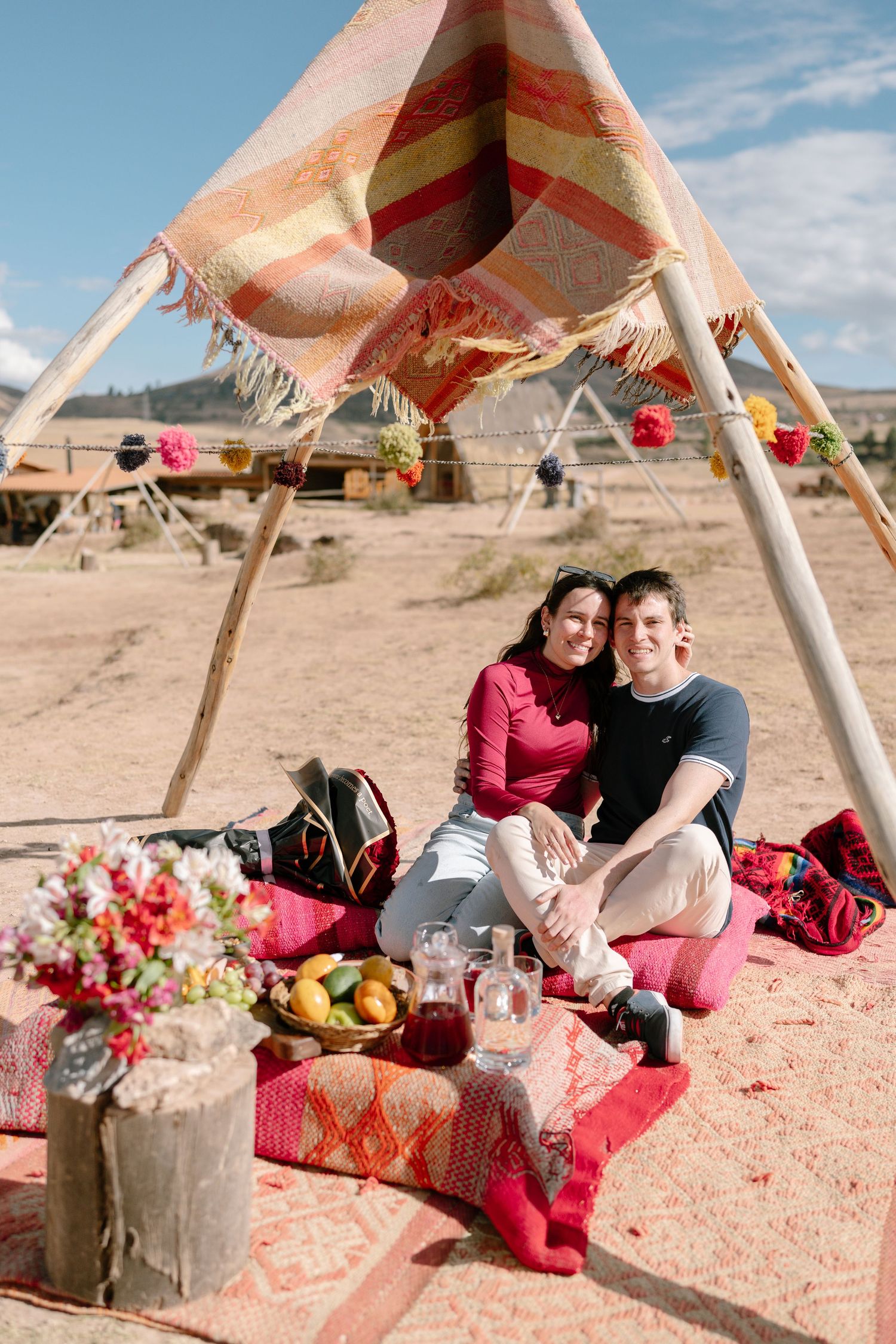 Romantic picnic setup under a boho tent with red roses and decorative details.