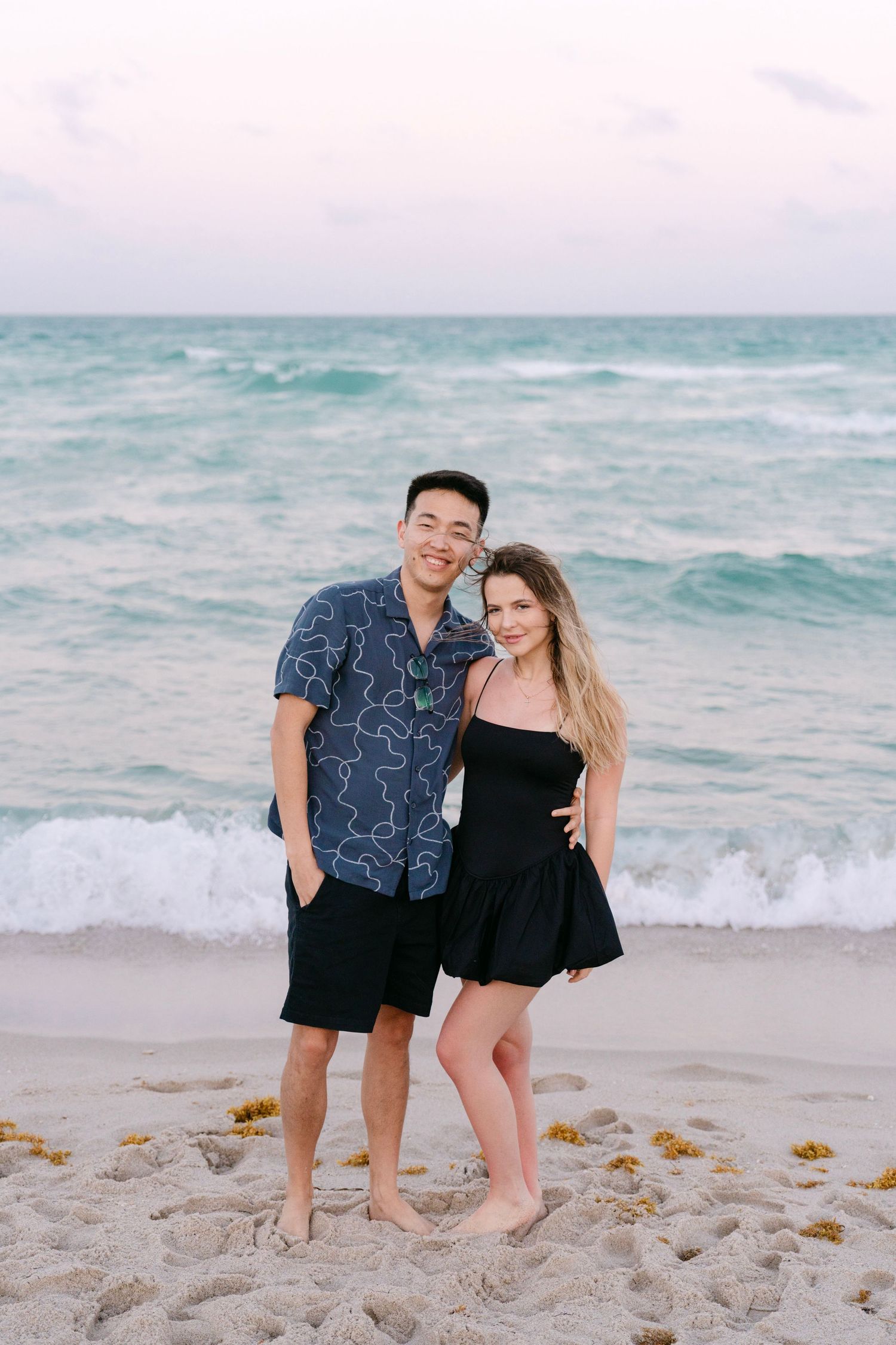 A couple wearing coordinated black outfits shares a joyful moment on the beach.