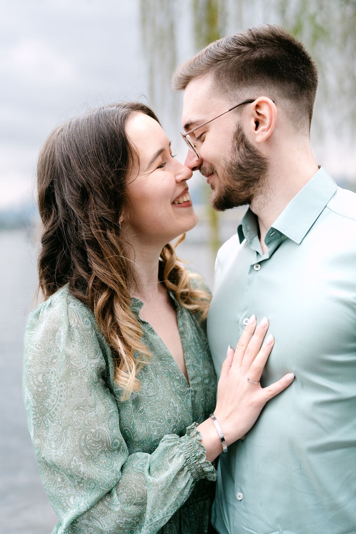 A couple in mint green and light blue outfits share an intimate moment by the water.