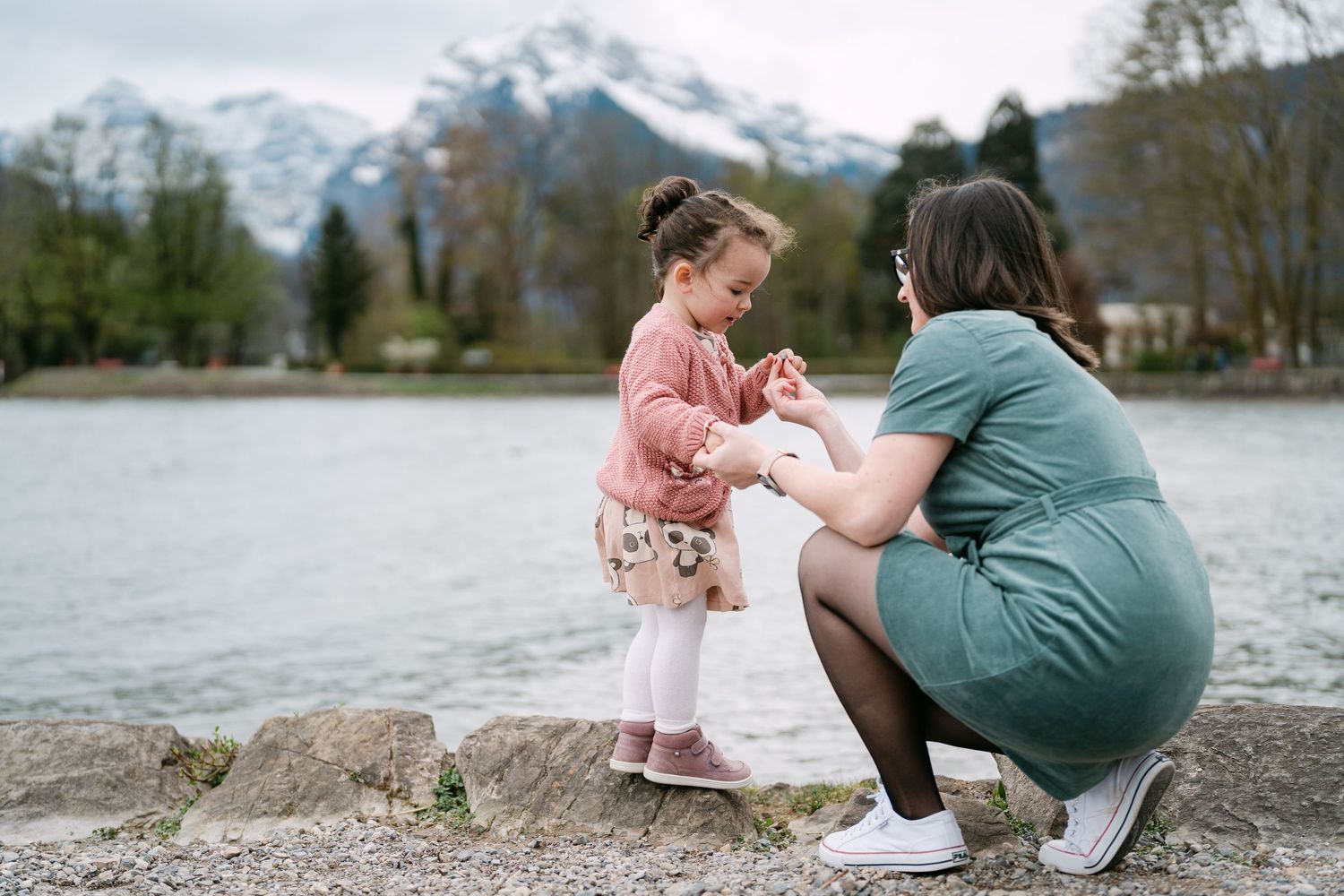 Family enjoying a peaceful moment by a lake with mountains in the distance.