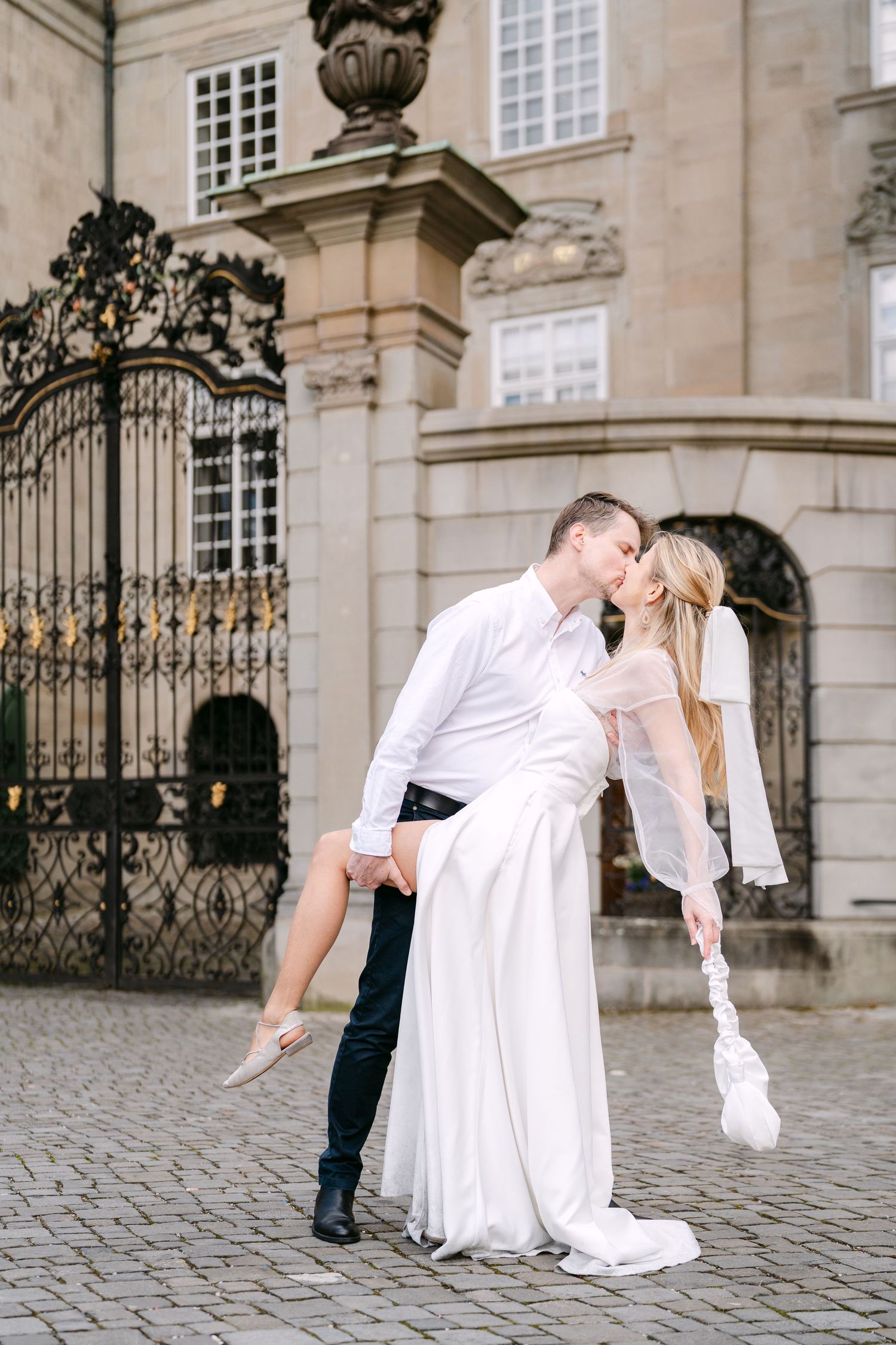 Couple in wedding attire sharing intimate moments on cobblestone courtyard near historic architecture.