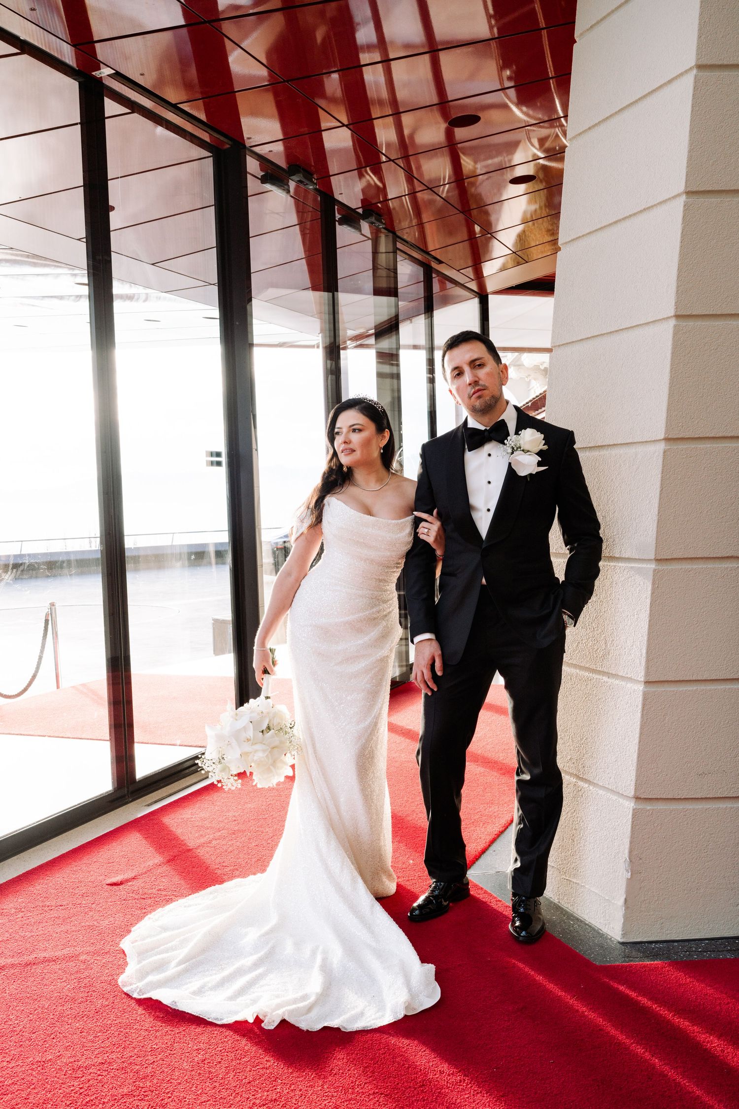 Wedding couple poses dramatically on red carpet in elegant venue hallway.