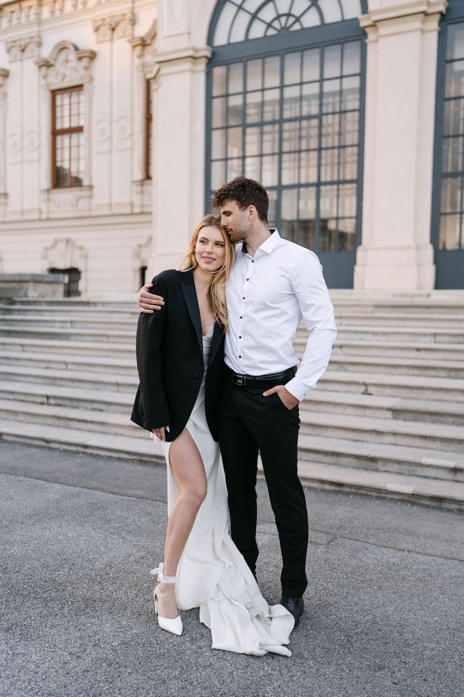 Stylish couple in formal wear posing on grand palace steps.