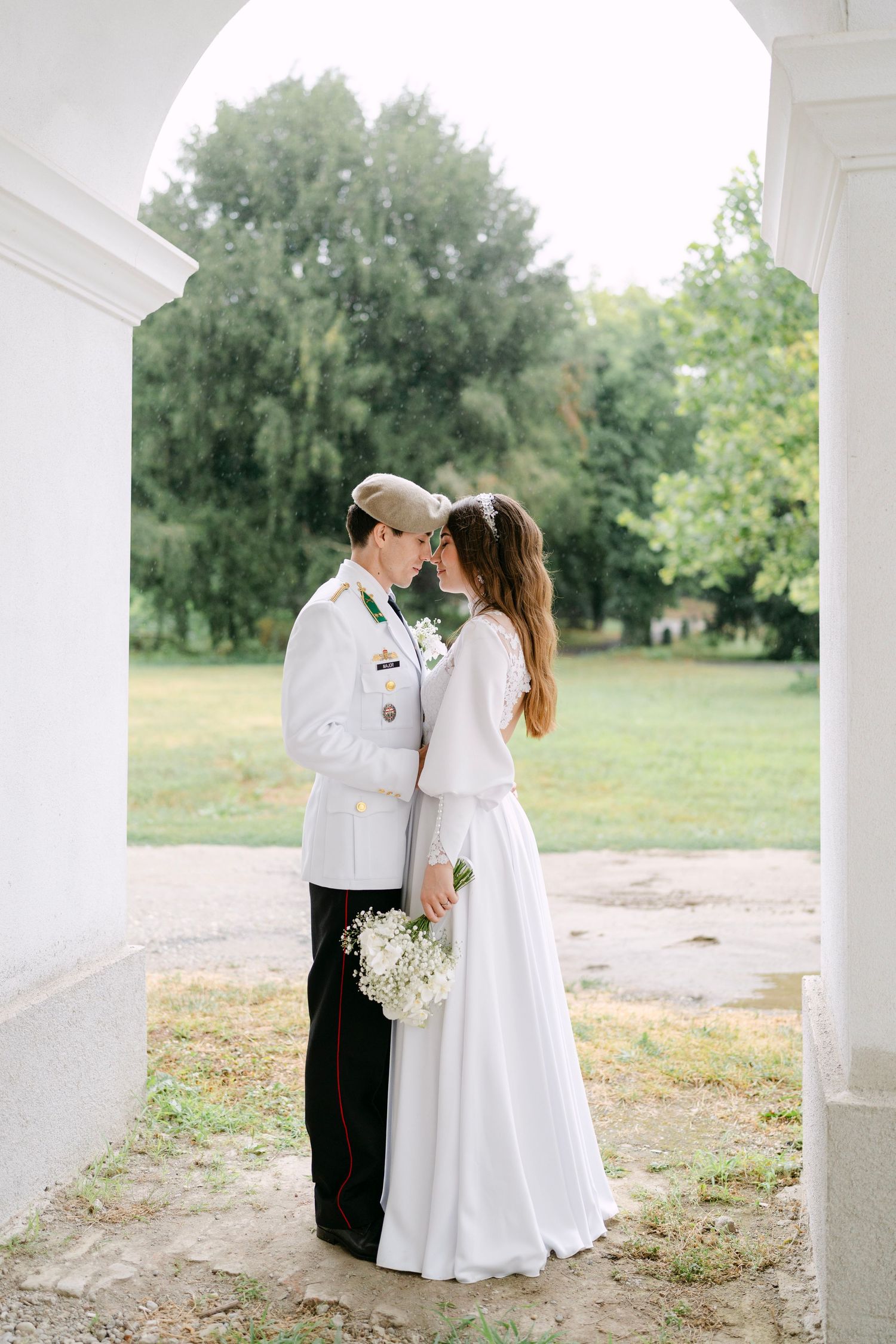 A romantic moment captured under white columns with a green landscape backdrop.