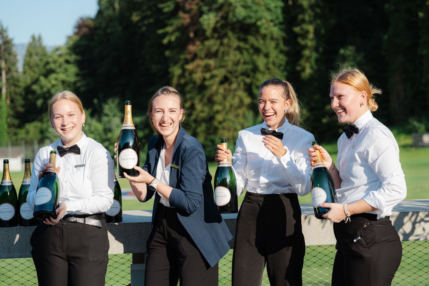Service team posing with Laurent-Perrier champagne bottles outdoors.