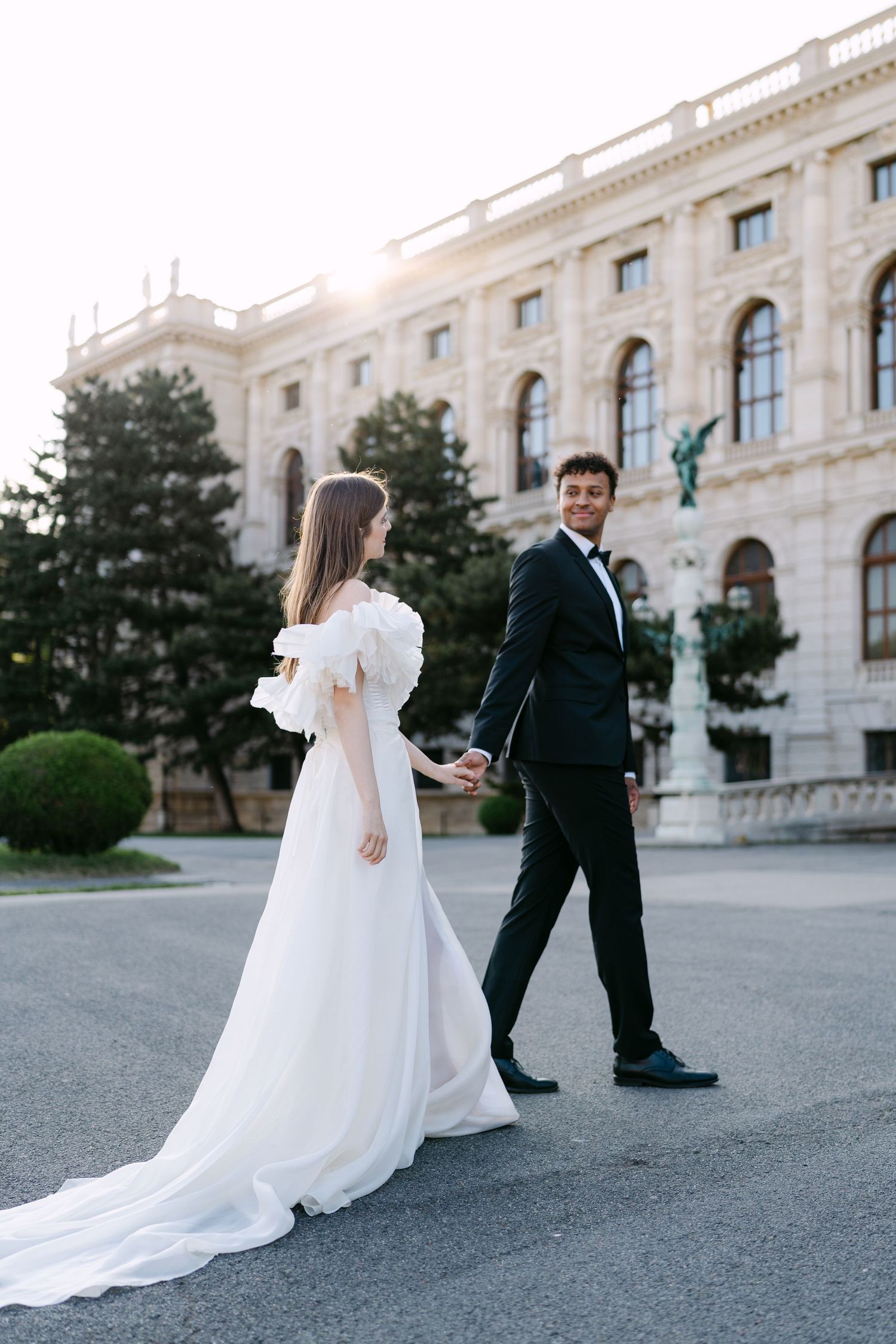 Wedding couple dances on stone pathway in front of grand historic building.