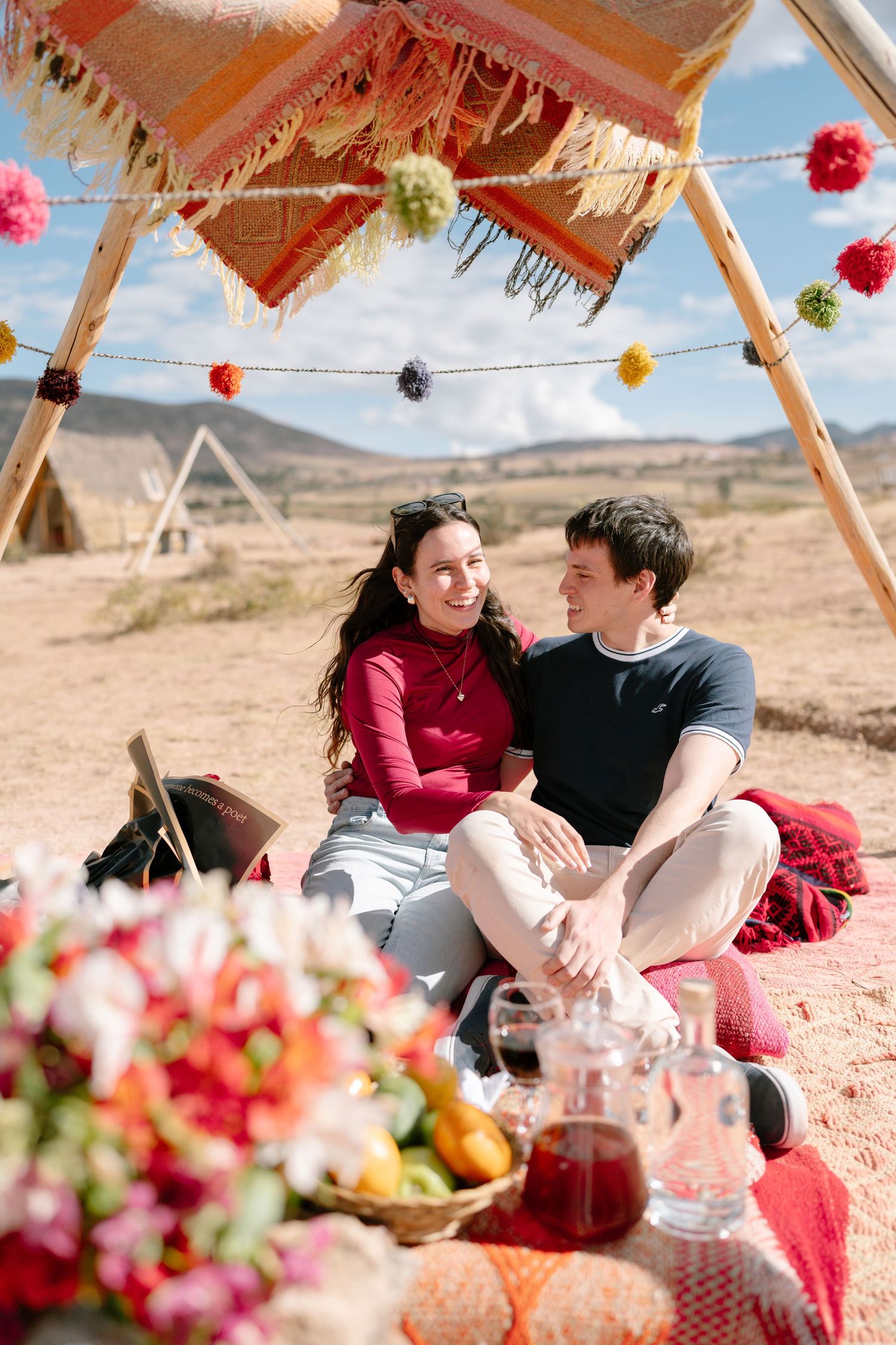 Couple enjoying a romantic picnic under a decorated tent with colorful pom poms.