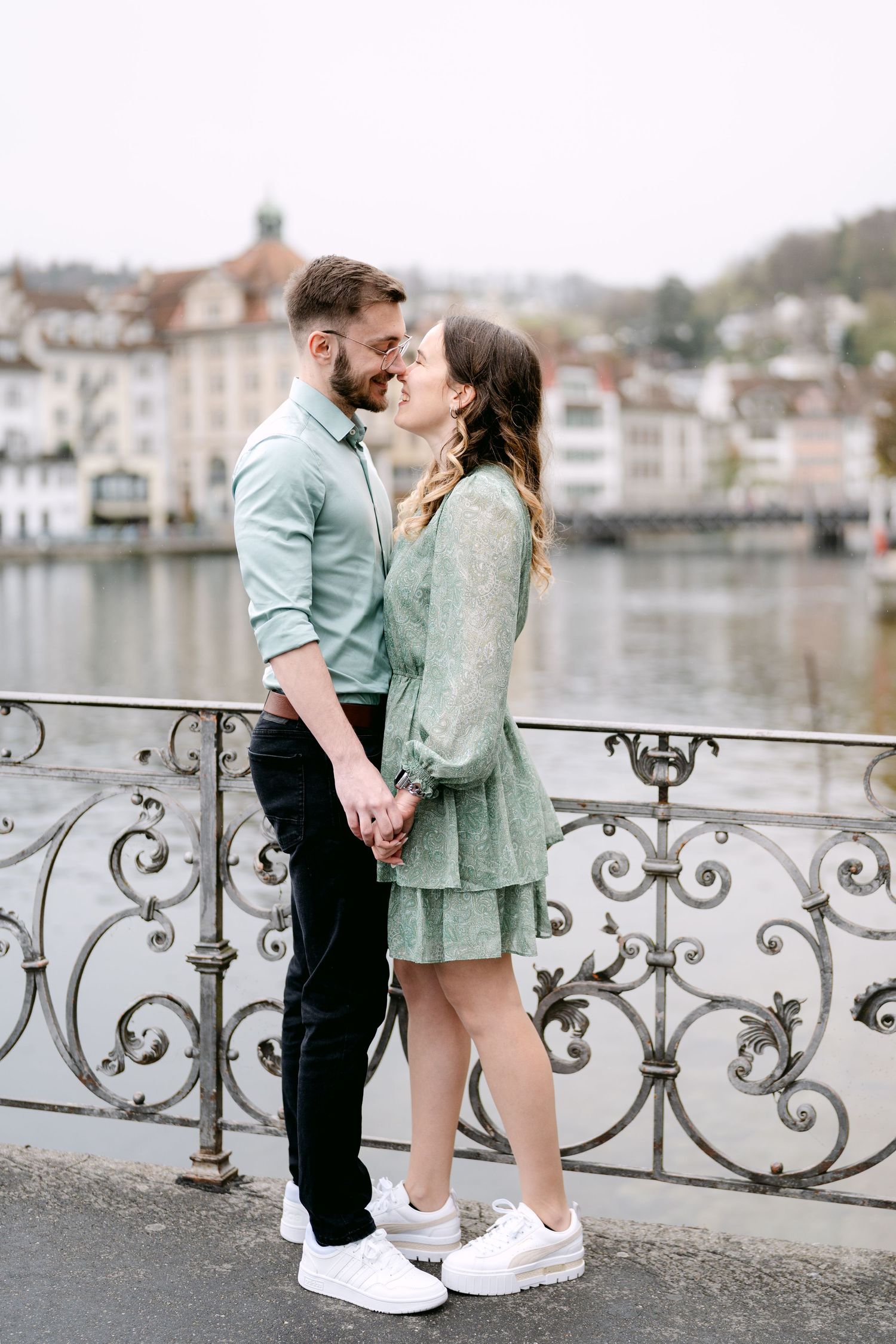 A couple shares an intimate moment on a decorative bridge railing overlooking a scenic waterway.