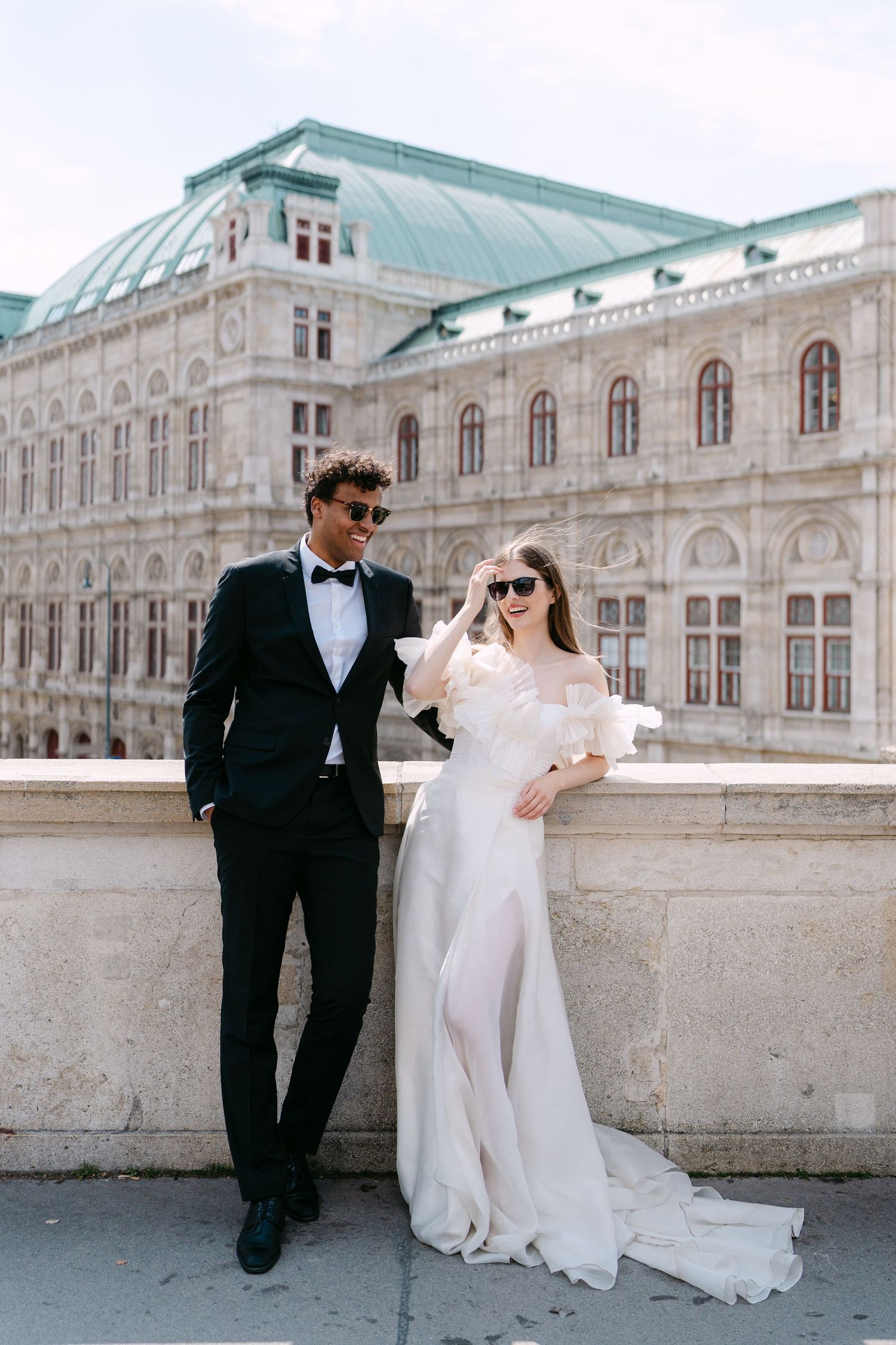 Elegant couple poses against Vienna State Opera's iconic architecture in classic black and white attire.