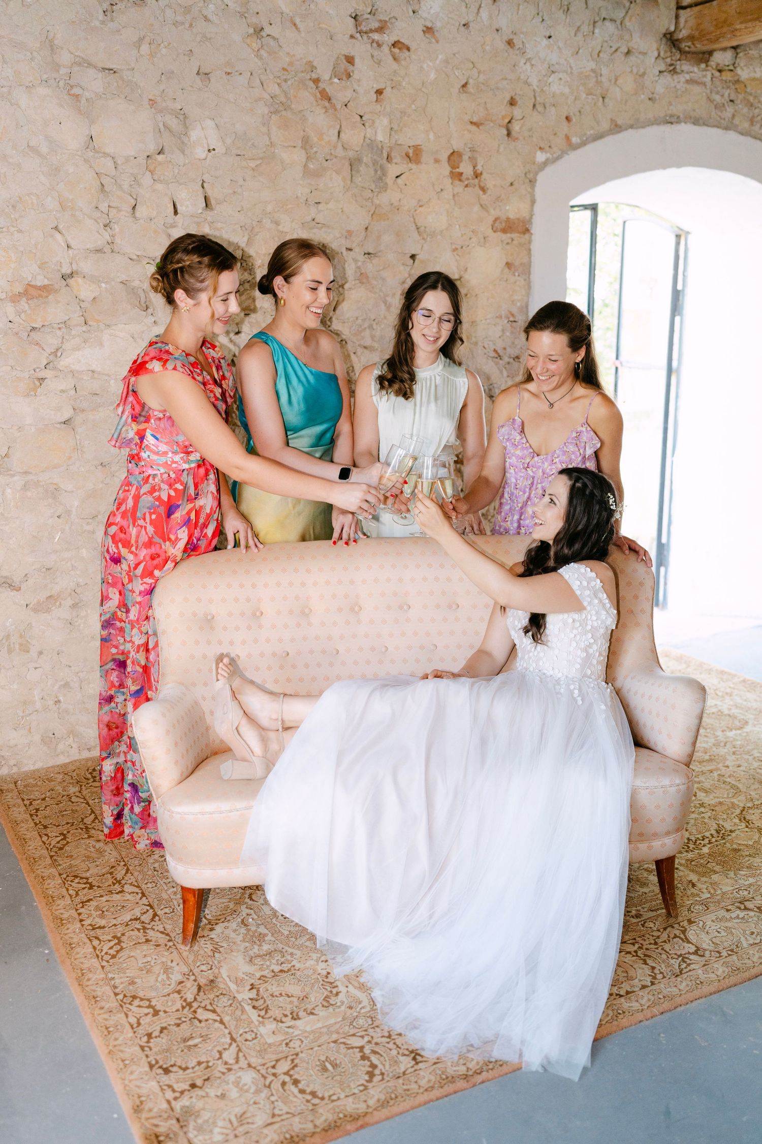 Candid moment of bridesmaids helping with a wedding dress on a vintage sofa.