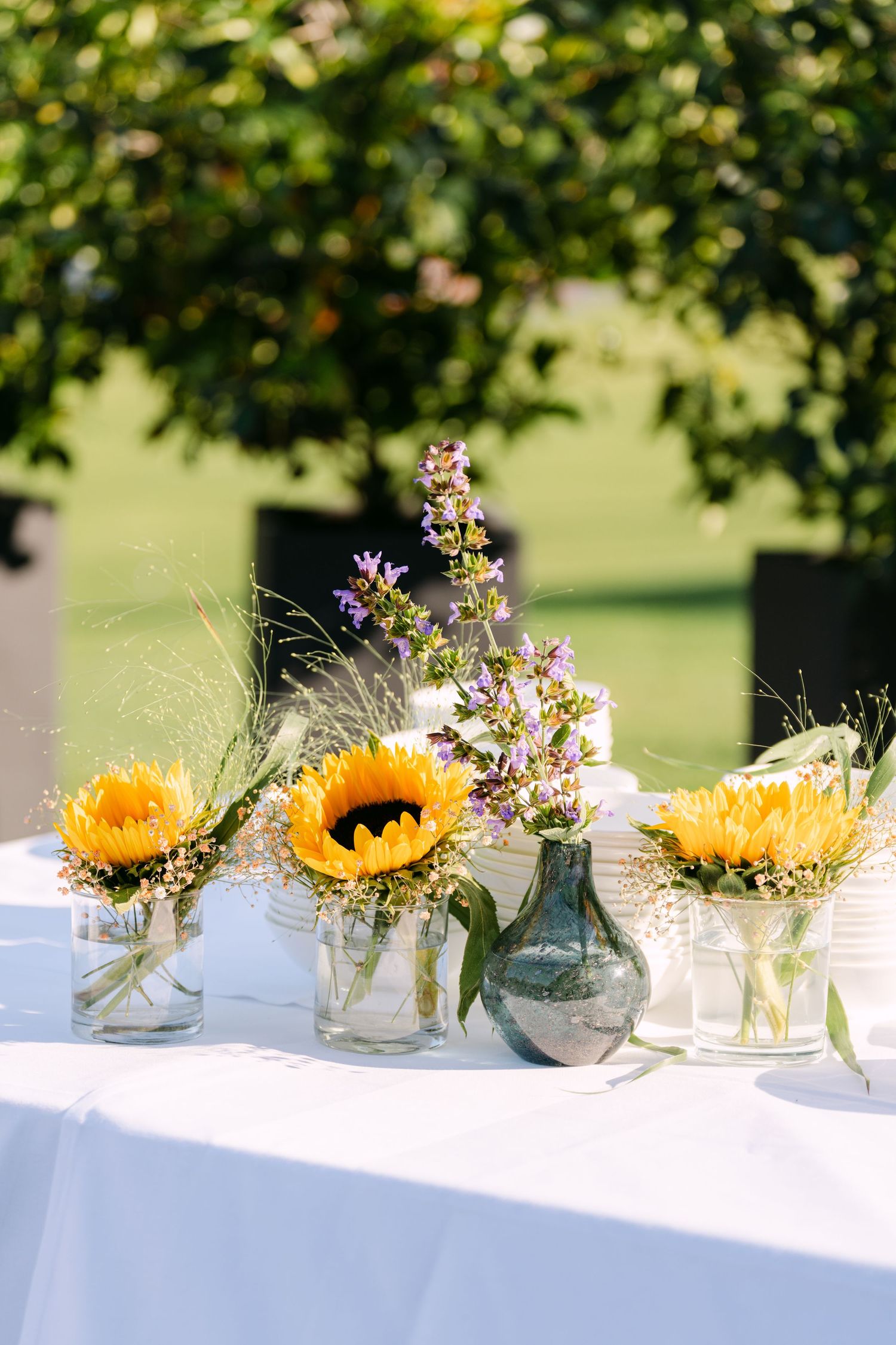 Sunflowers and wildflowers in glass vases arranged on a white tablecloth outdoors.