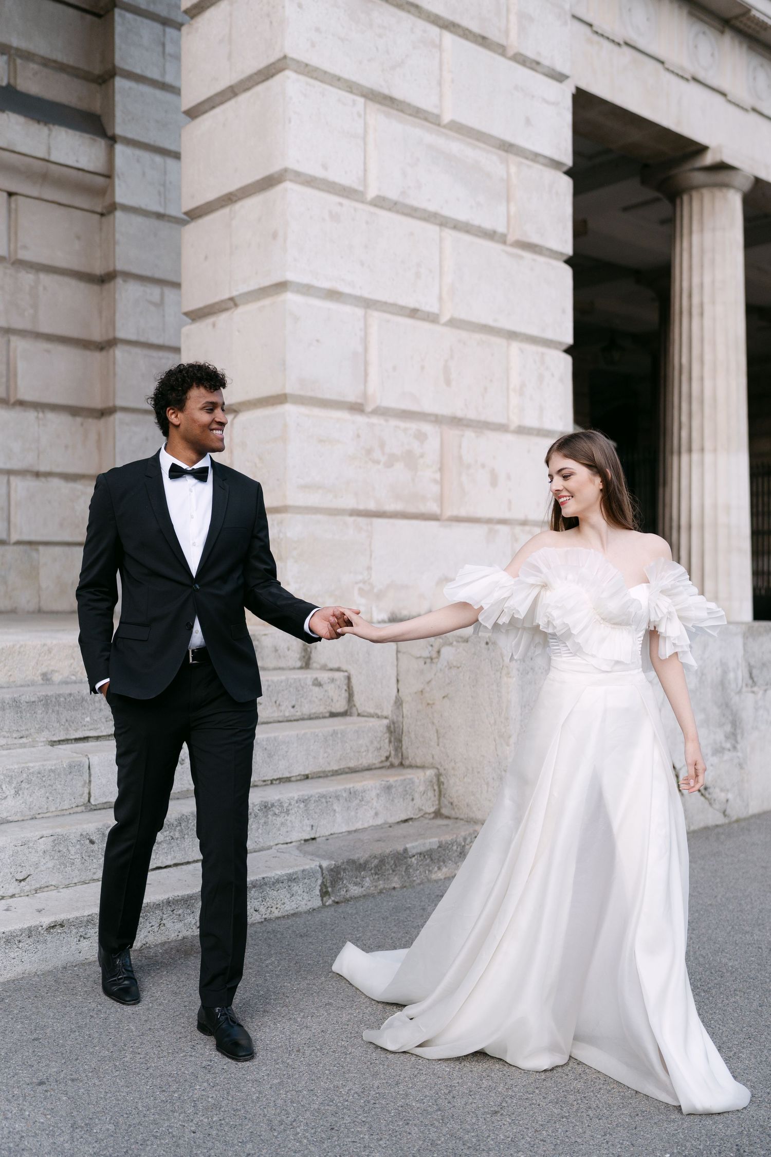 Elegant wedding couple playfully poses on stone steps in black and white formal attire.