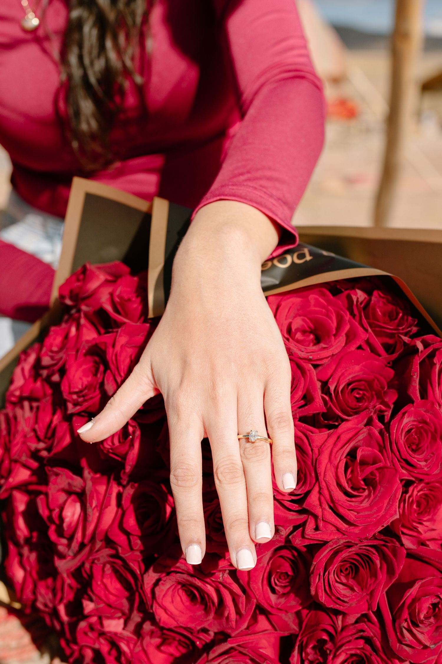 Close-up of a hand with an engagement ring resting on vibrant red roses.
