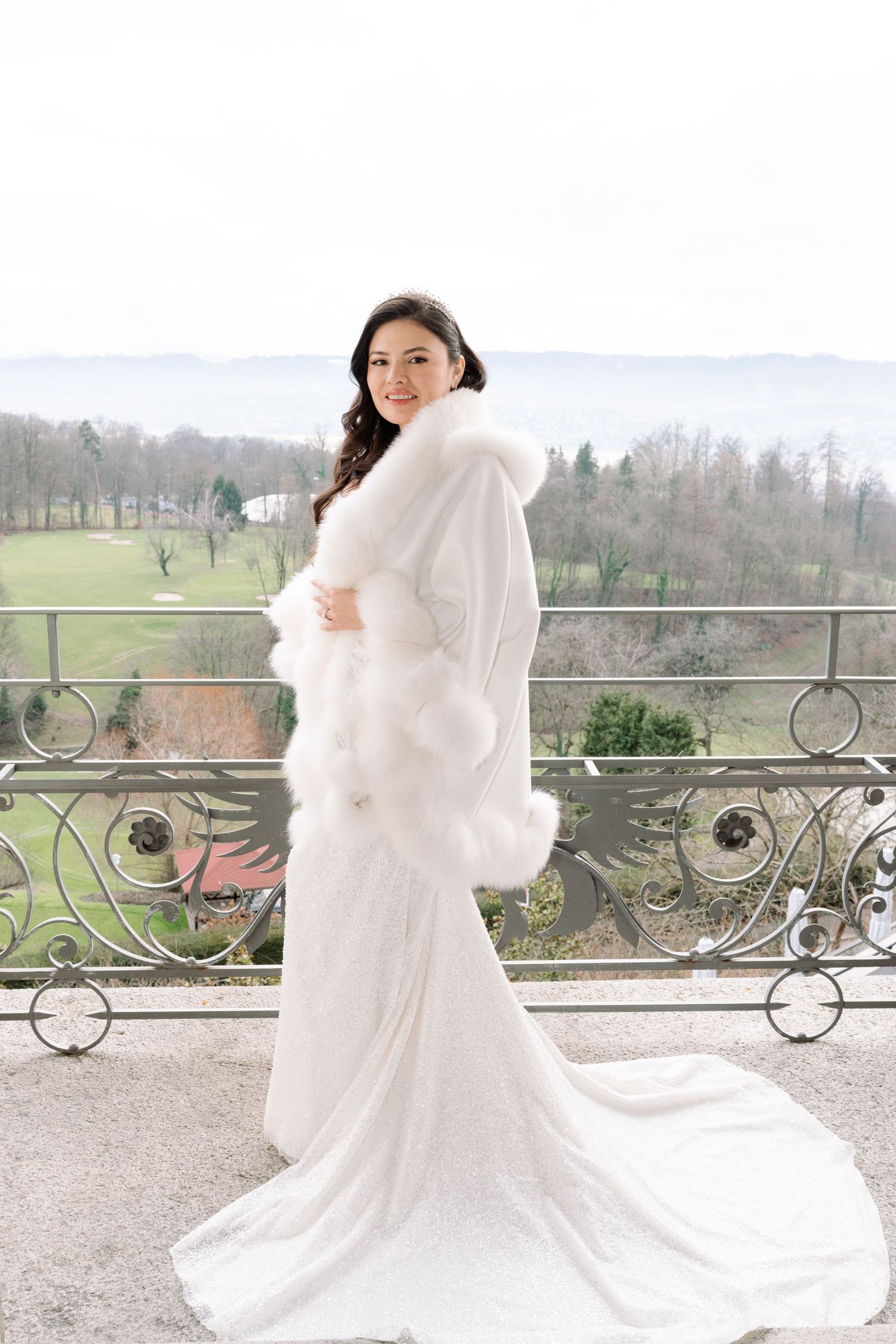 Wedding dress flowing in breeze on elegant balcony overlooking scenic landscape.