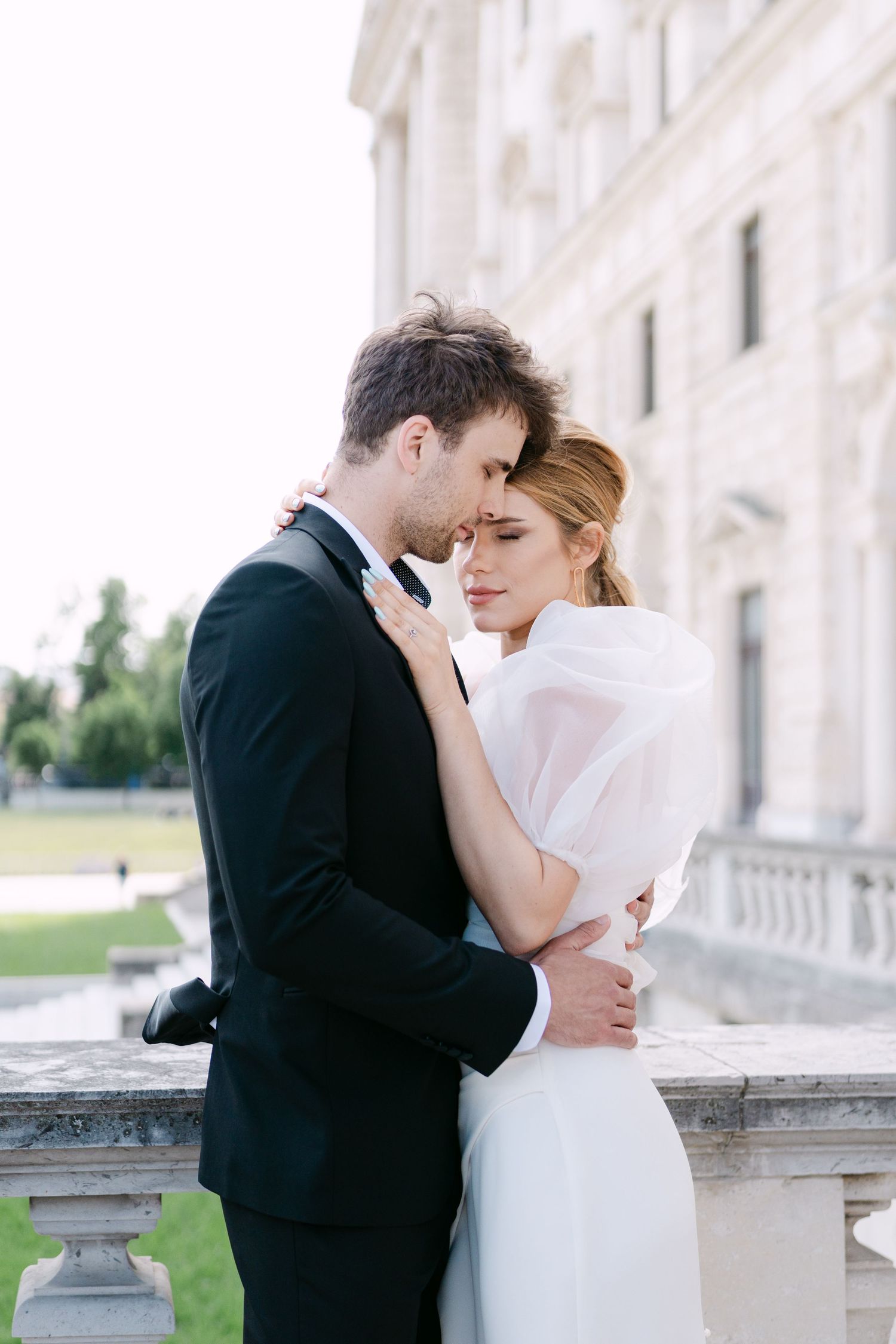 Elegant wedding couple embracing on a grand balcony of a historic building.