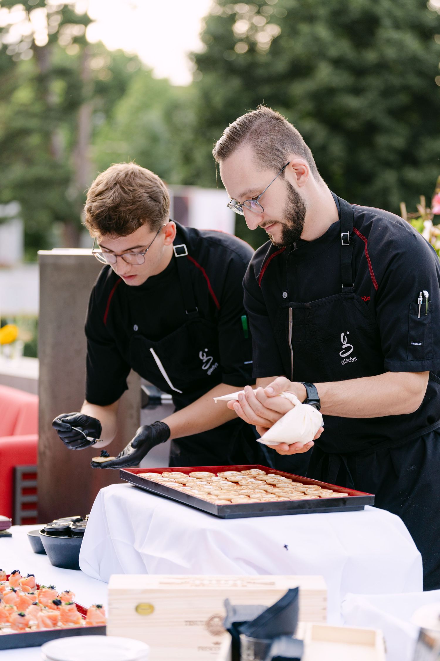 Catering staff in black uniforms preparing food at an outdoor serving station.