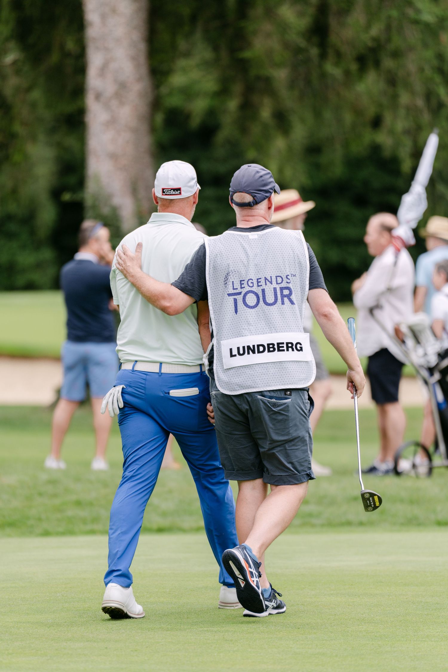 Golf caddies and players walking across a manicured tournament green.