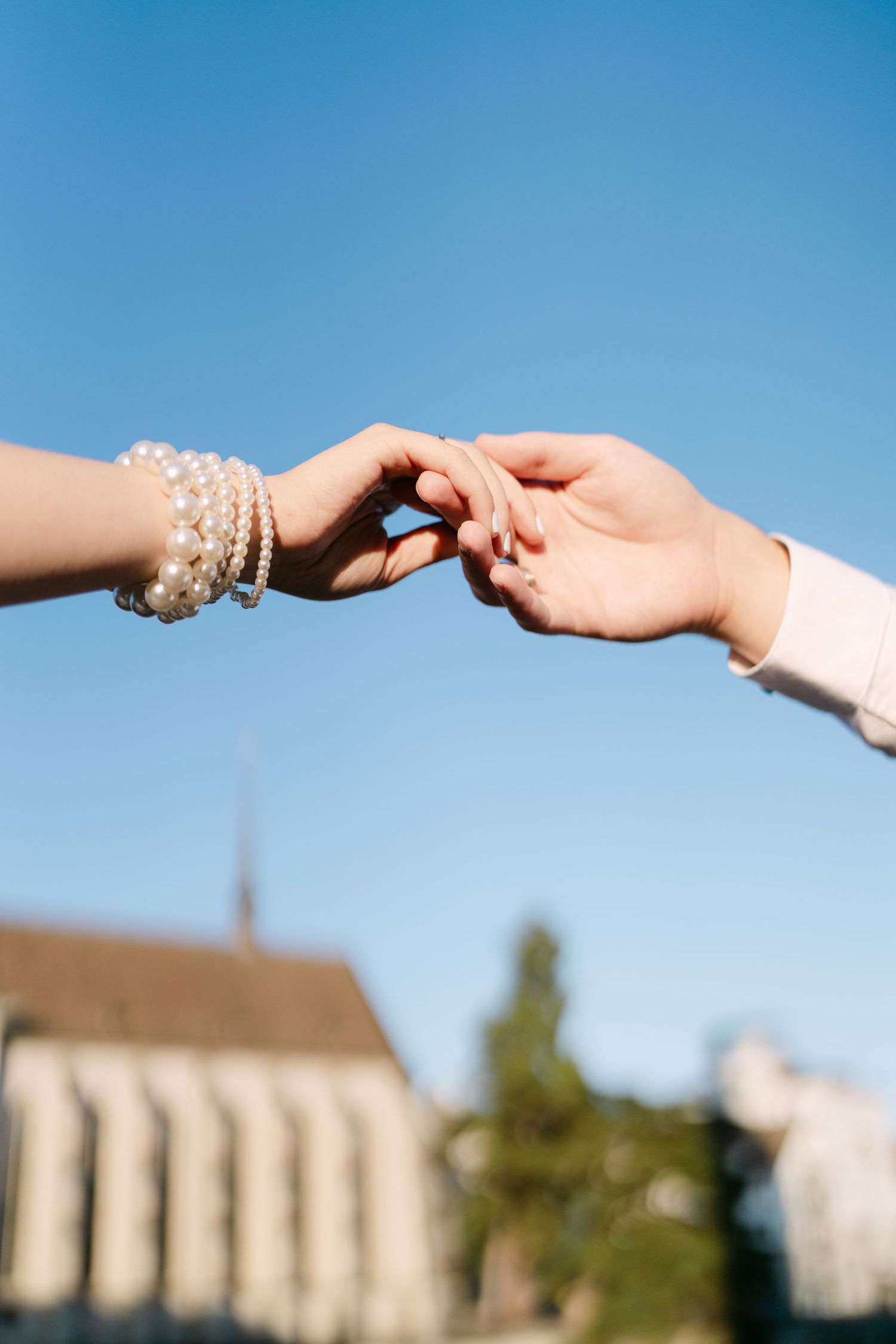 Hands reaching towards each other against a bright blue sky with buildings in the background.