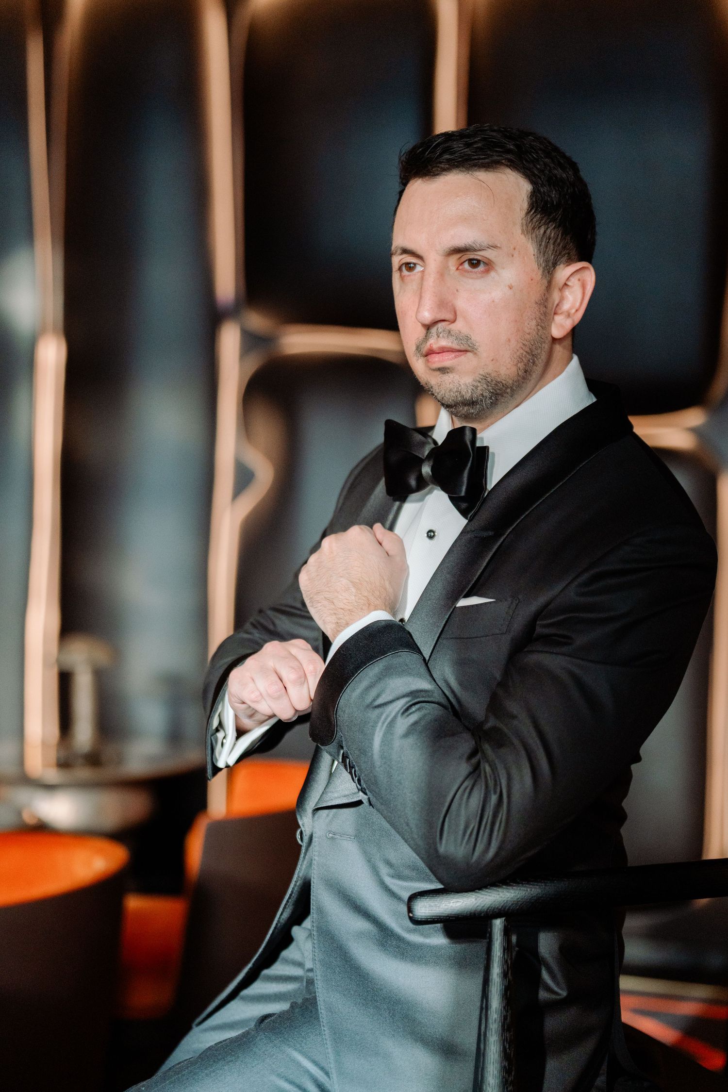 Groom in classic black tuxedo poses against modern copper-toned interior.
