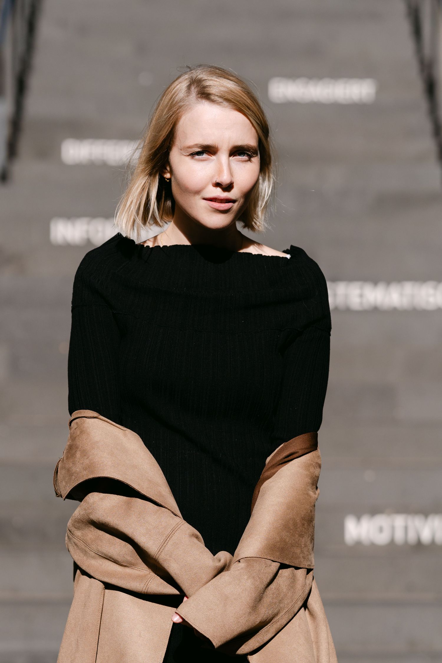 Fashion portrait series showing contrasting black dress and tan coat against concrete background.