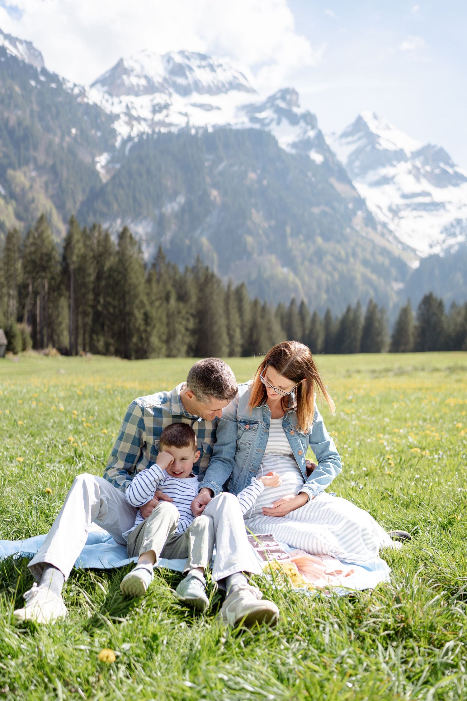 Family relaxing on blanket in alpine meadow with dramatic mountain backdrop.