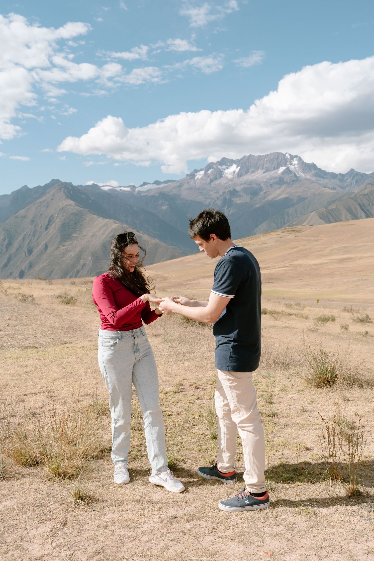 A couple playfully interacts in an open field with mountain views.