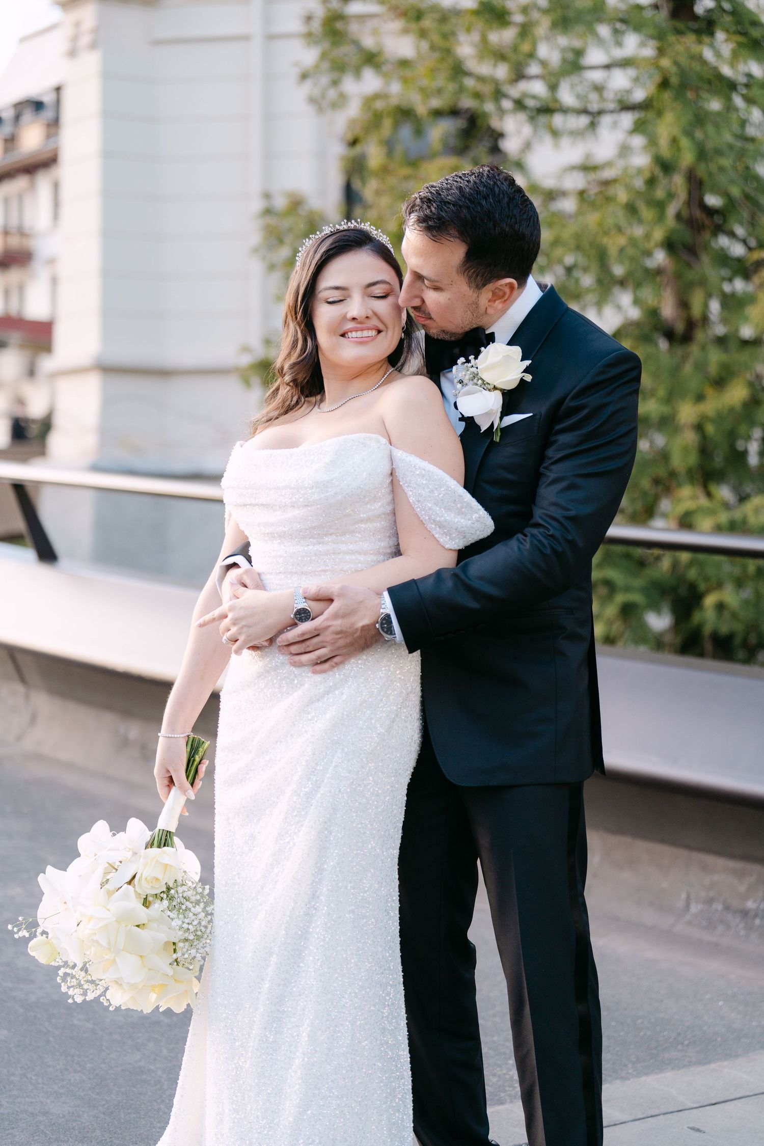 Romantic wedding couple embracing on outdoor terrace with white floral bouquet.