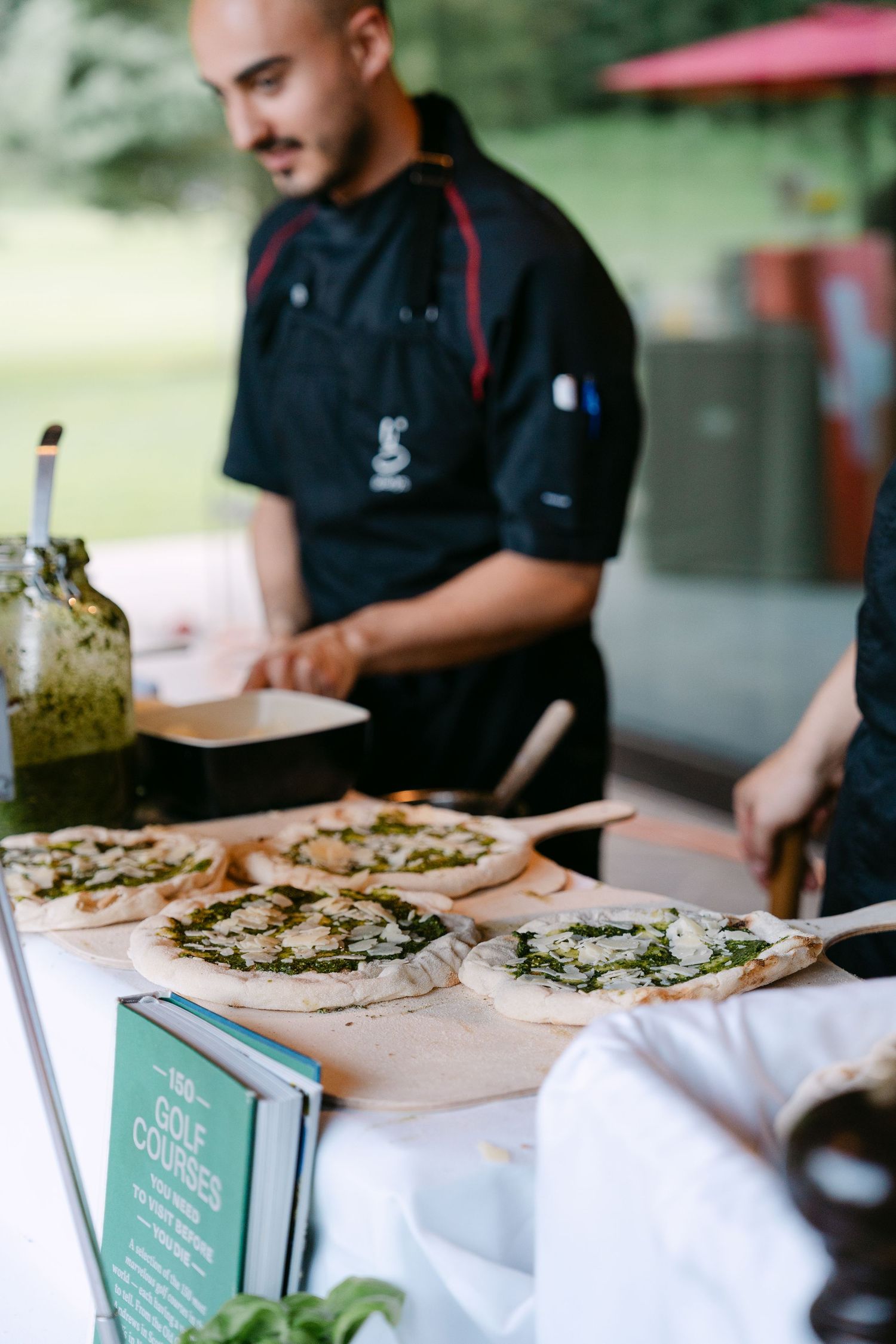 Flatbreads topped with pesto sauce being prepared at an outdoor catering station.