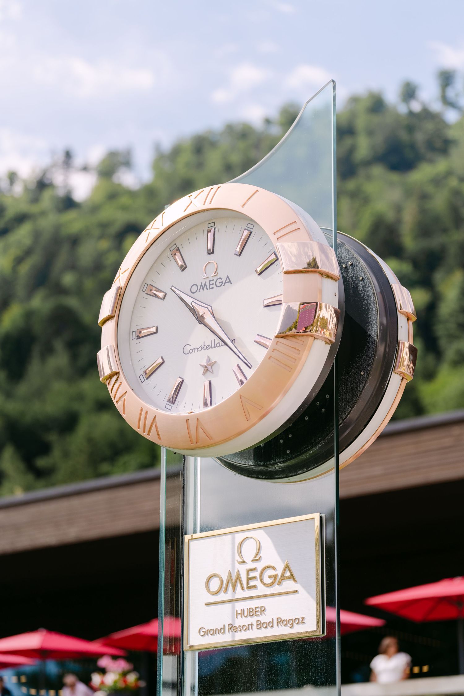 Large Omega watch display installation with rose gold timepiece against mountain landscape.