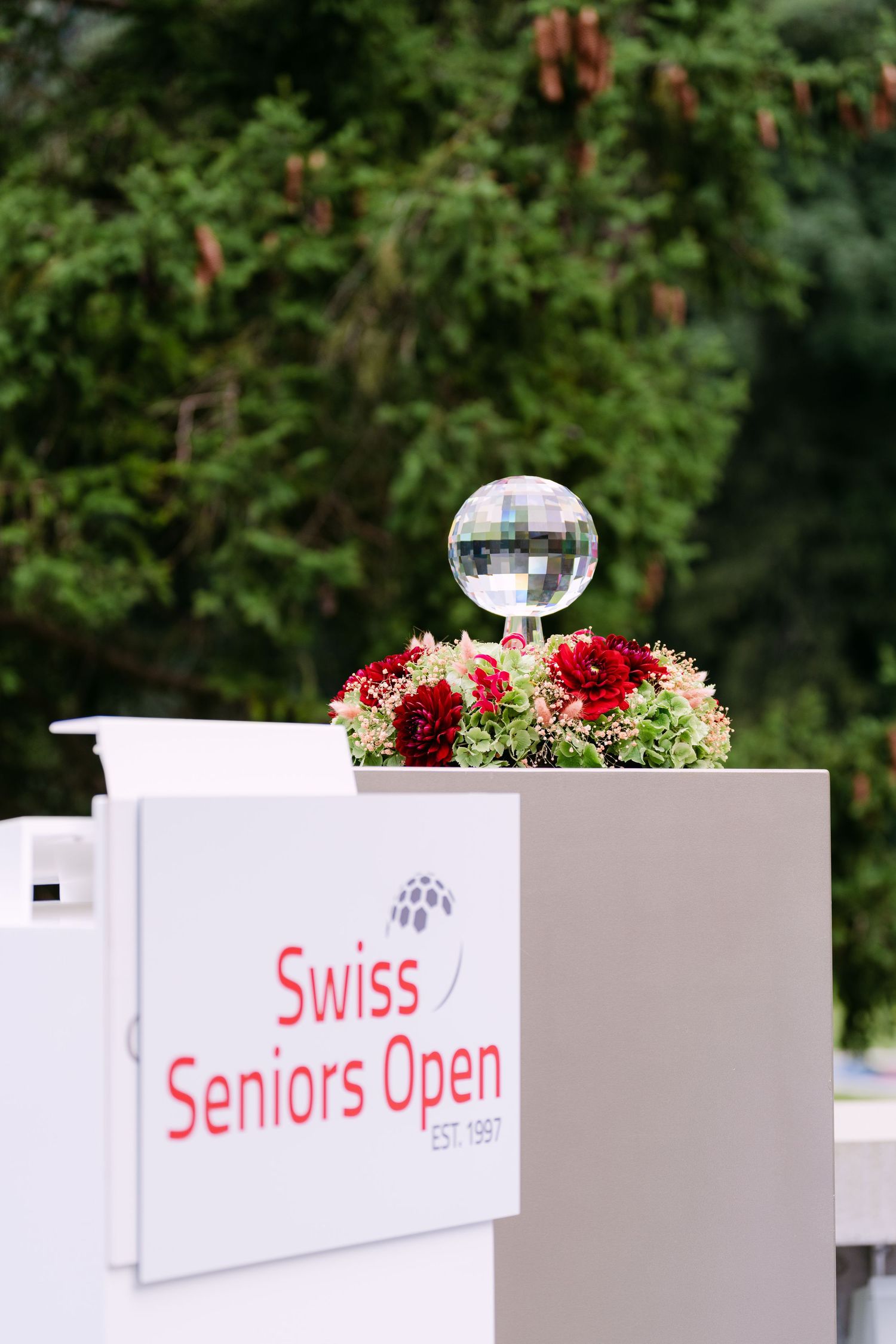 White decorative signage for Swiss Seniors Open with red floral arrangements.