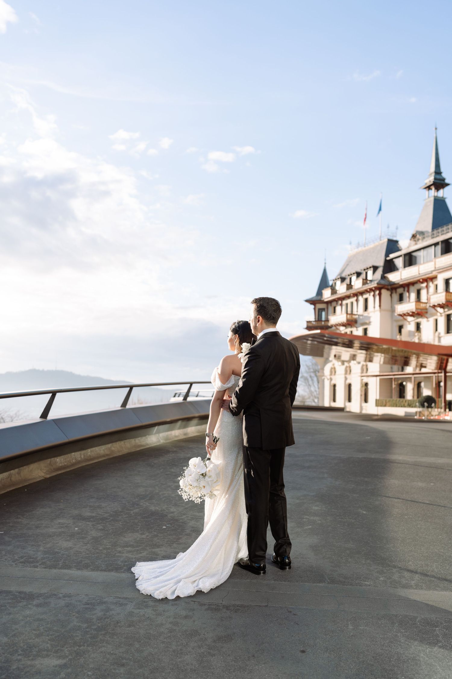 Newlyweds pose against stunning mountain backdrop at luxury Swiss hotel.