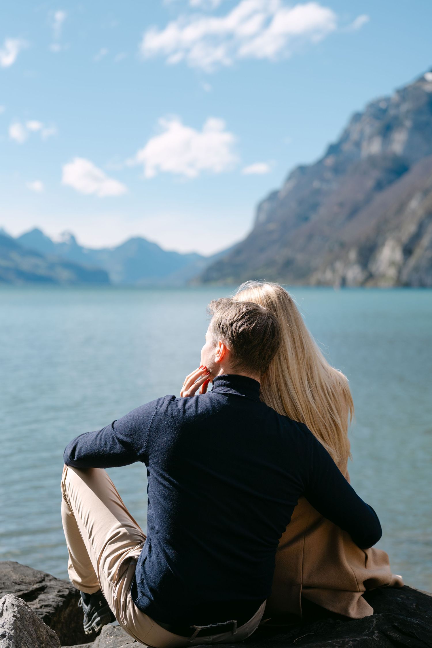 Intimate moments shared on rocky shore with mountain lake vista.