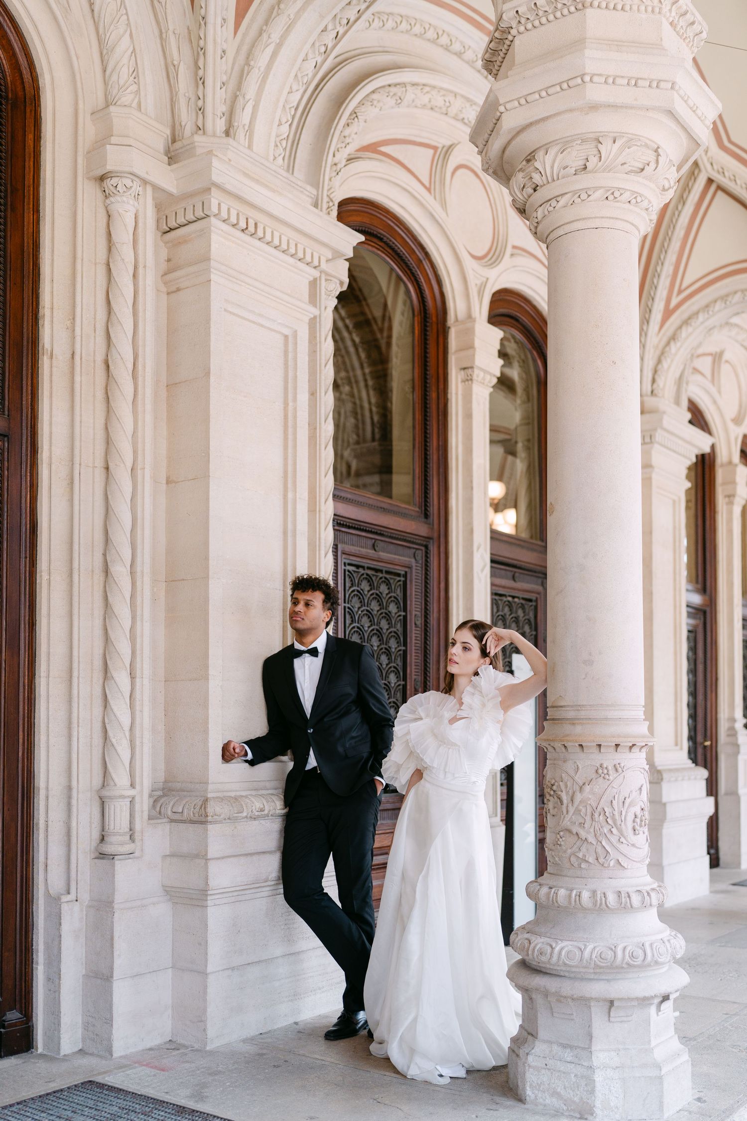 Bride and groom playfully interact among decorative white stone columns.
