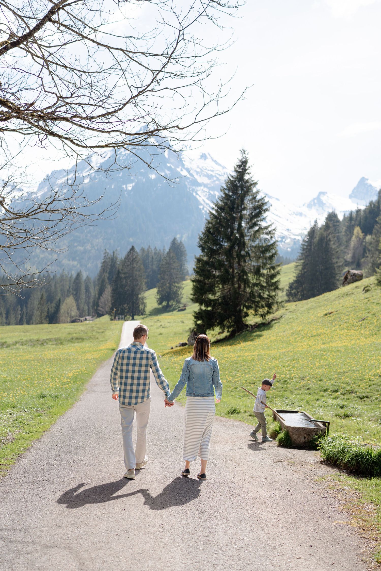 Three people stroll down a scenic mountain path surrounded by Alpine meadows.