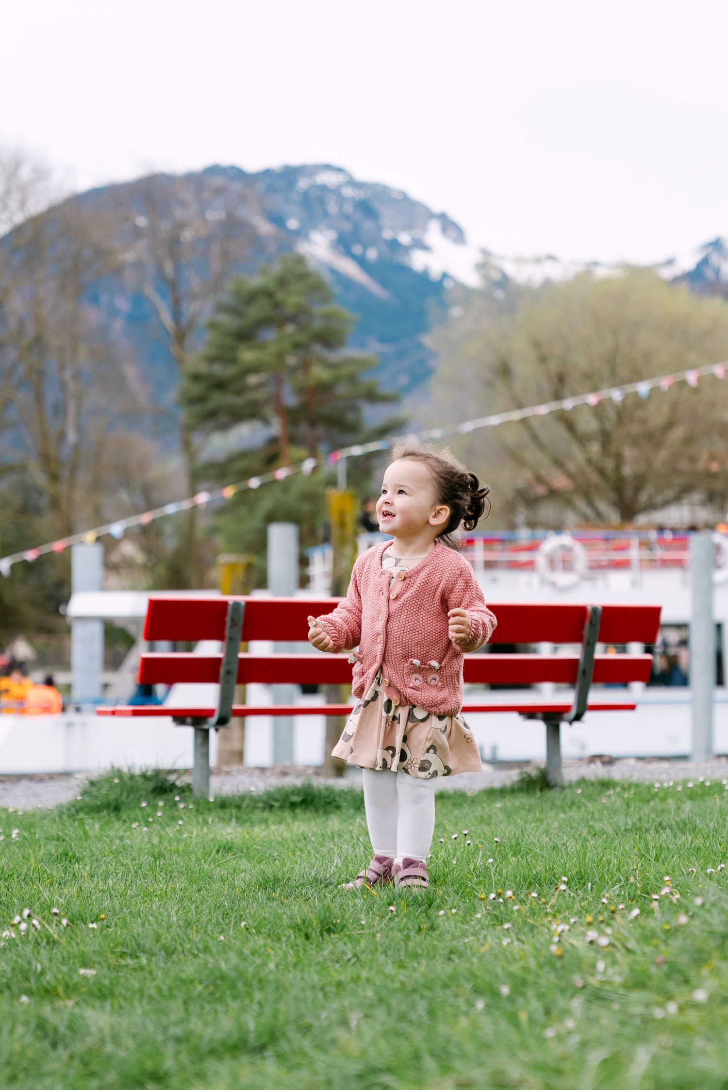 Child in pink running and playing on grass with mountains in background.