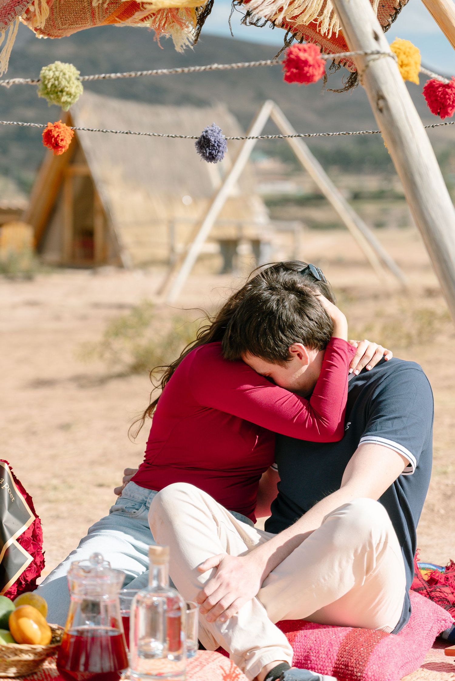 Cozy desert picnic setup with string lights and colorful pom poms hanging from wooden structure.